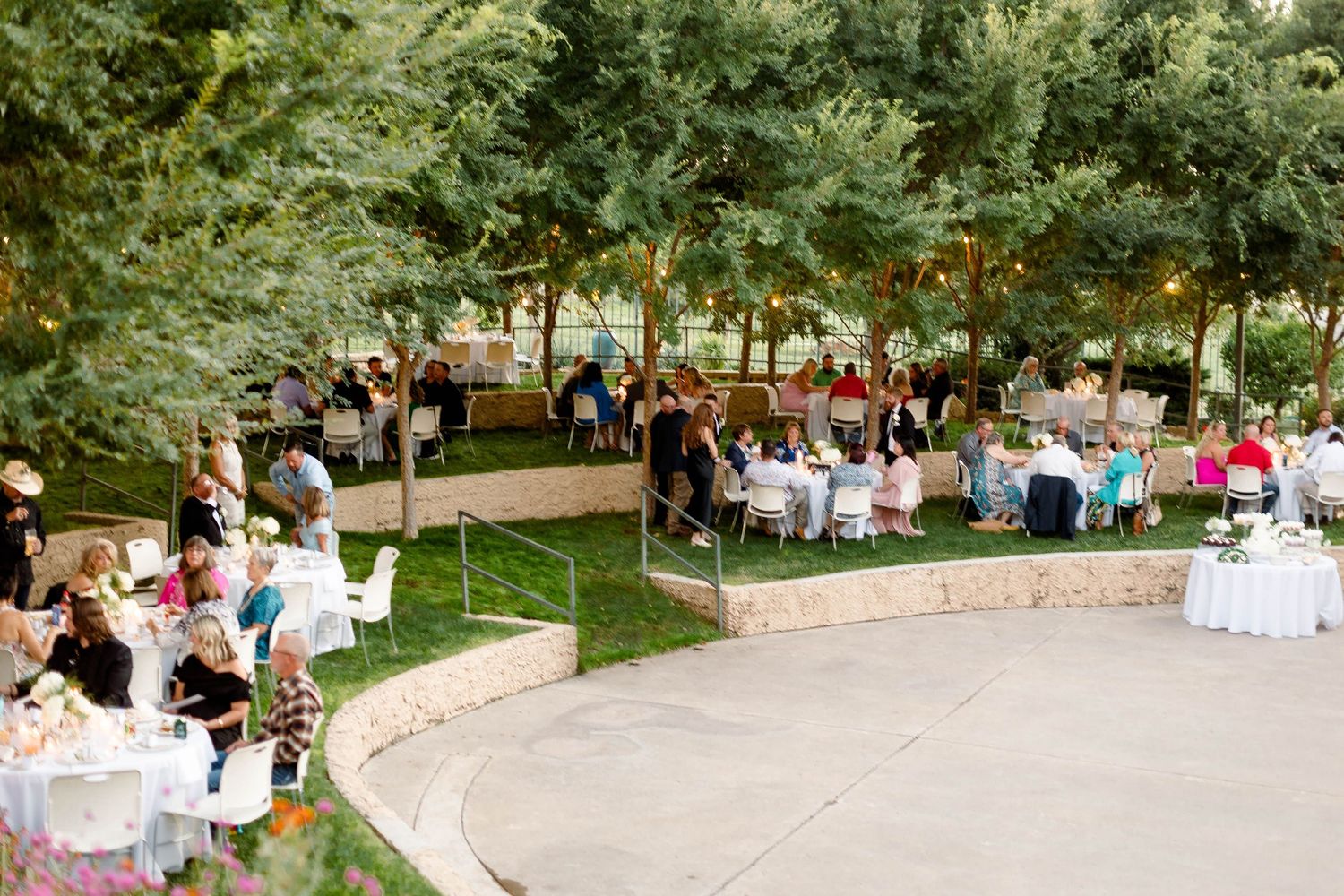 Wide view of an outdoor wedding reception with tables set up in a garden setting.