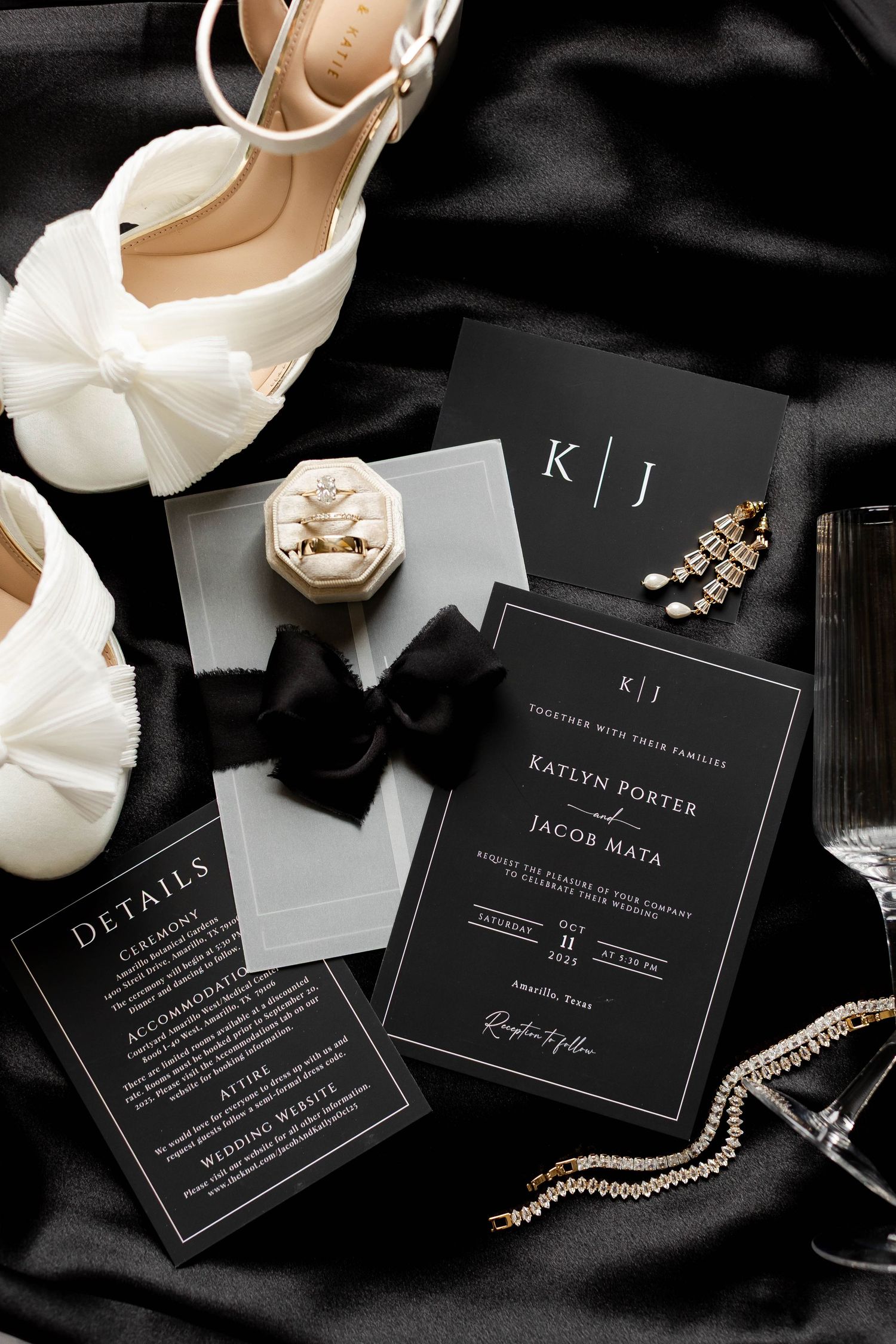 Elegant black and white wedding invitation suite with bridal shoes and jewelry accessories on dark fabric.