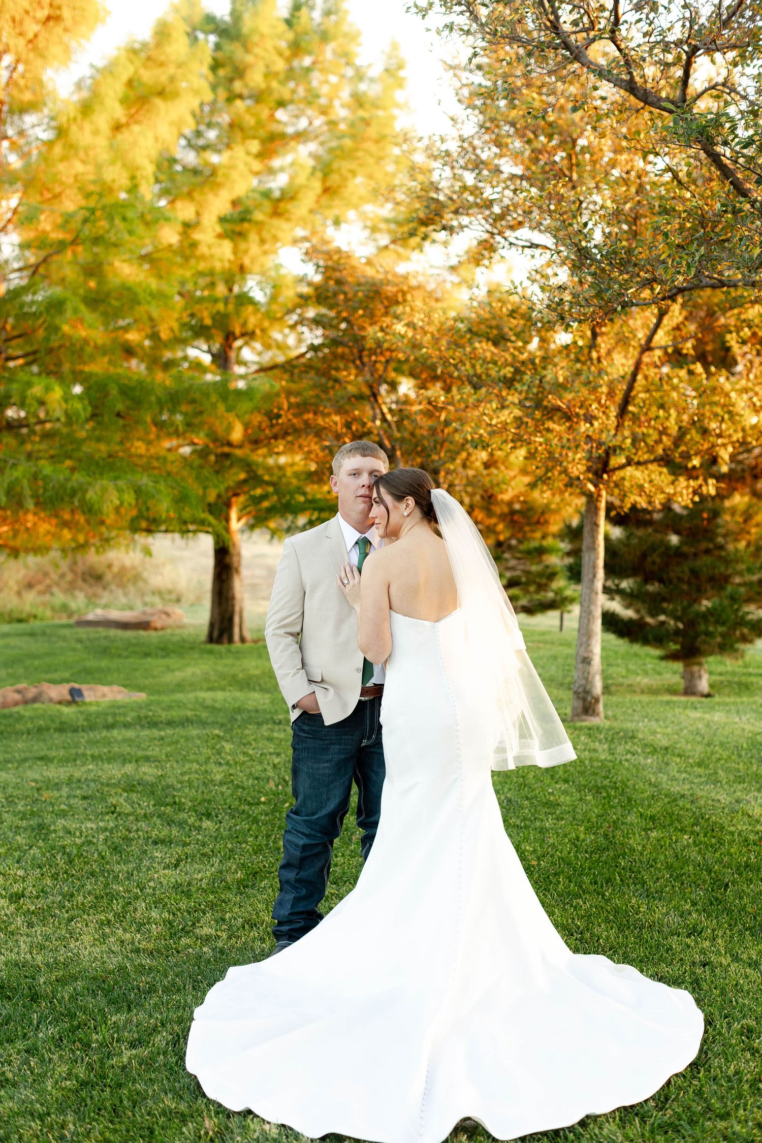 A romantic outdoor wedding photoshoot in a park with golden autumn trees and lush green grass at sunset.
