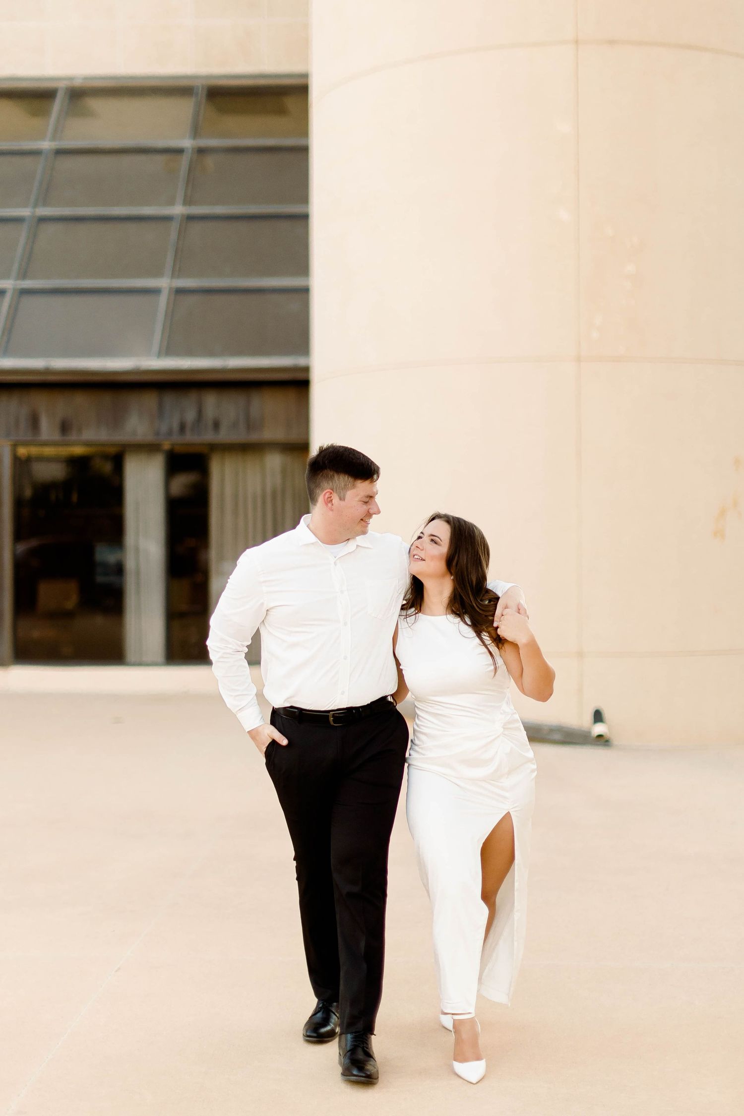 A couple in contrasting black and white outfits dance together on a beige-toned patio.