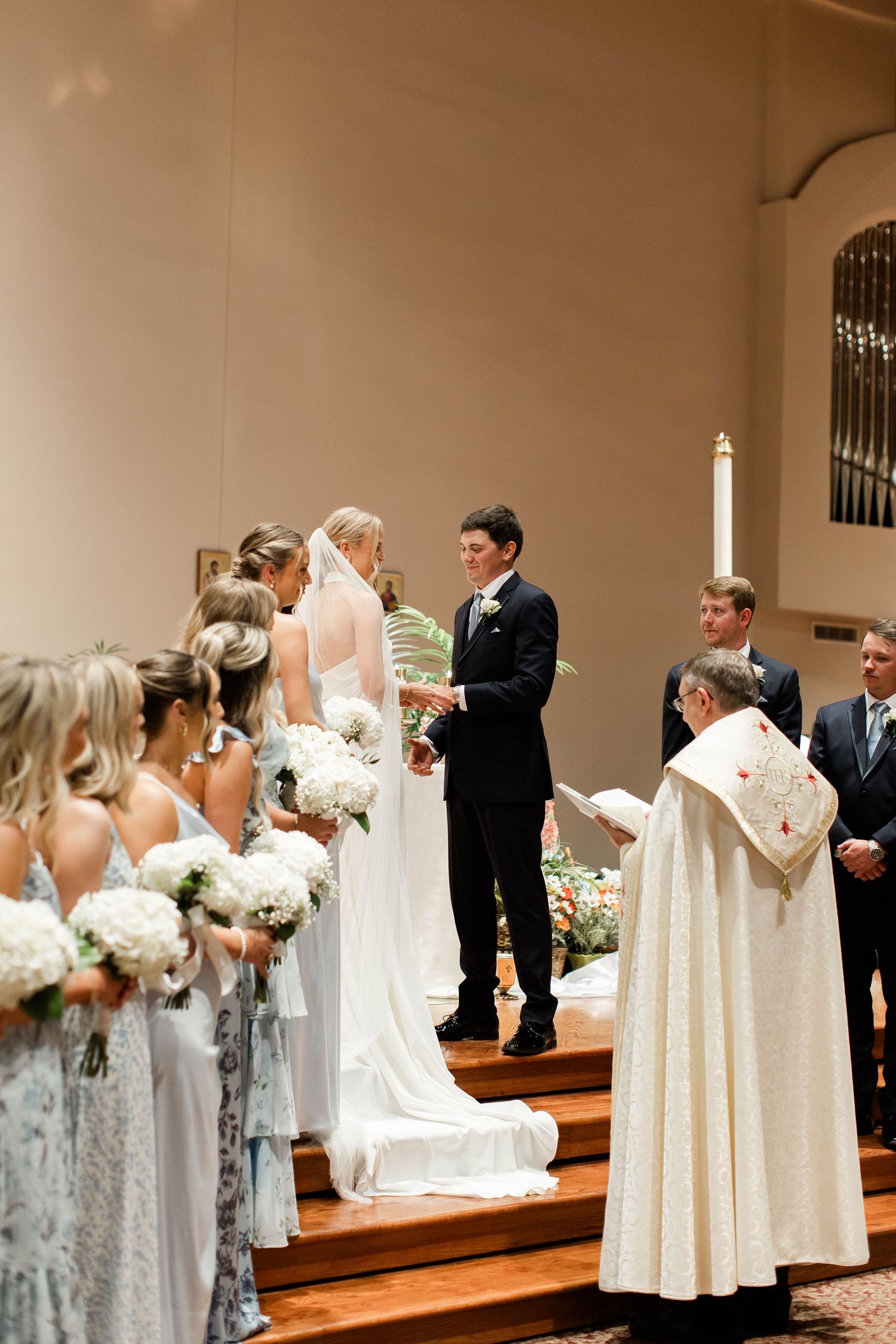 Wedding party arranged on church steps with bridesmaids in light blue dresses holding white bouquets.