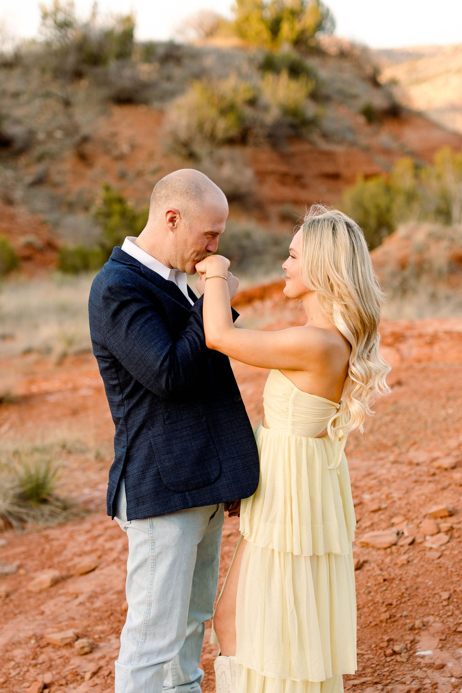 A romantic gesture between a couple in formal wear against a desert backdrop.