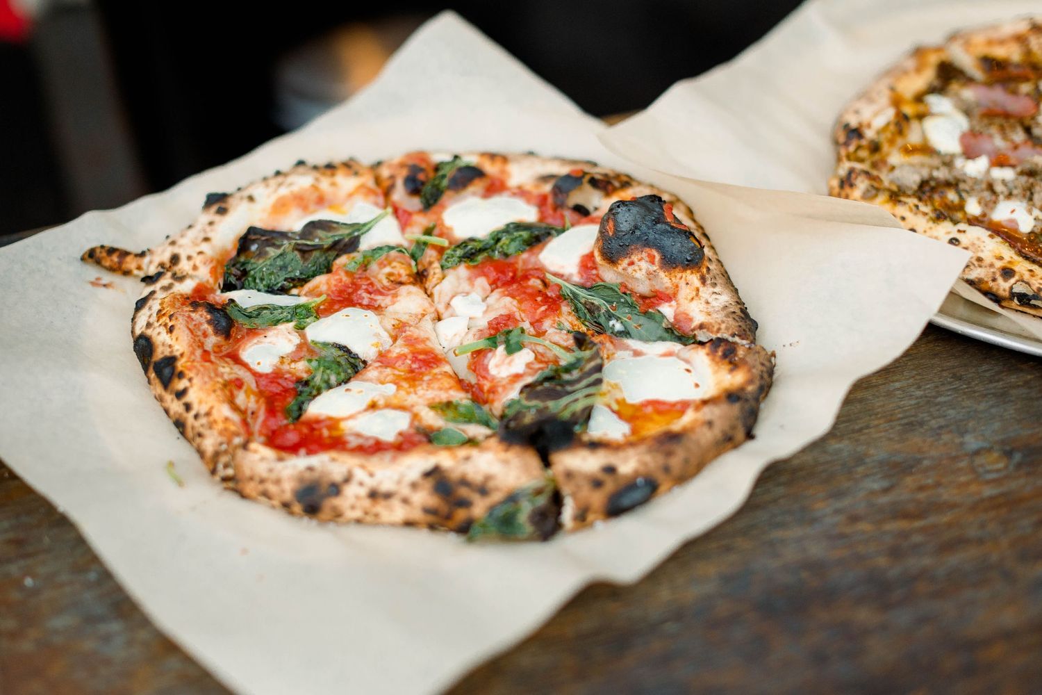 A Neapolitan margherita pizza cooking in a wood-fired oven shows stages of transformation from raw to perfectly charred.