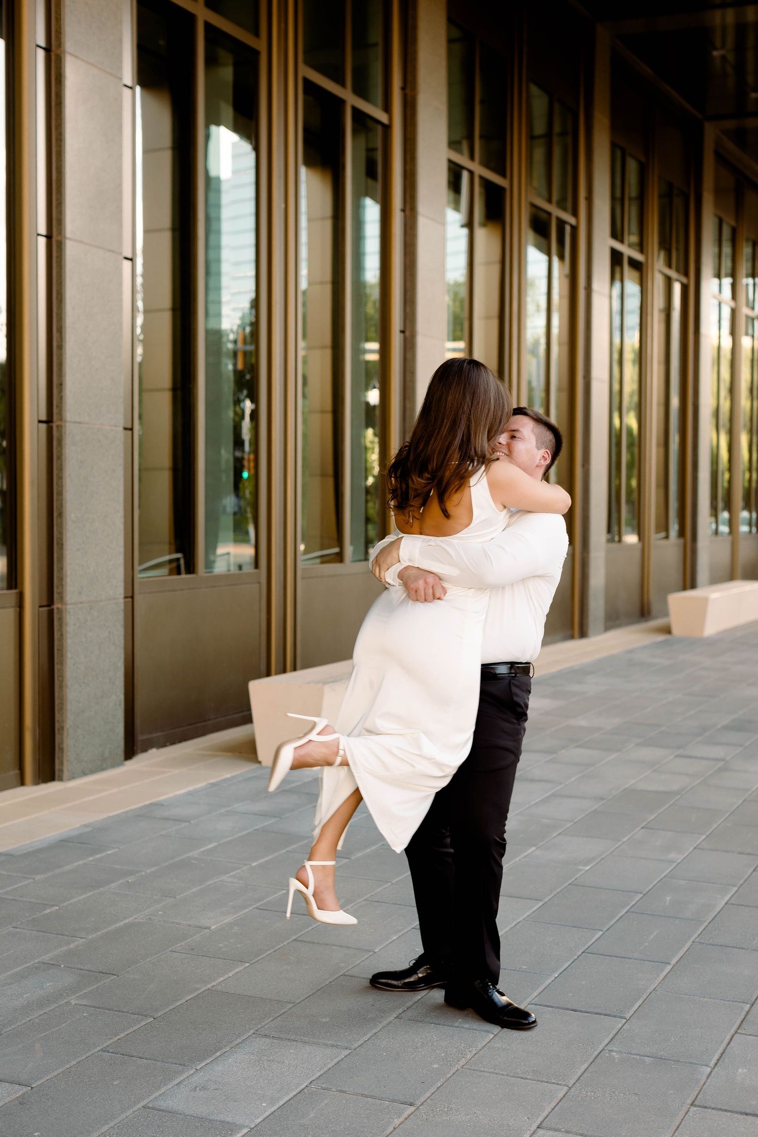 Dancing couple spins together in front of a modern building with glass windows.