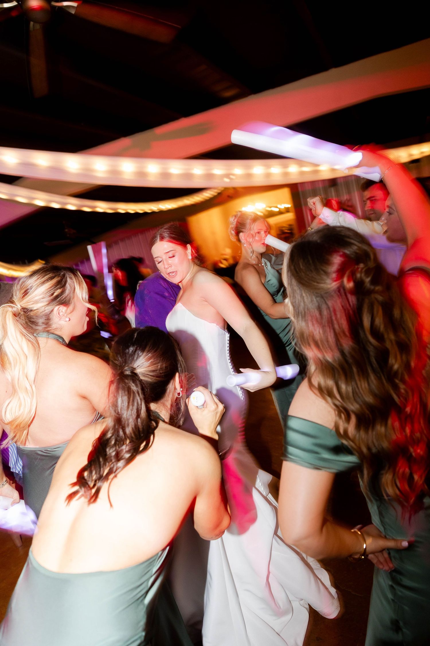 Wedding reception dance floor filled with guests dancing under colorful lighting.