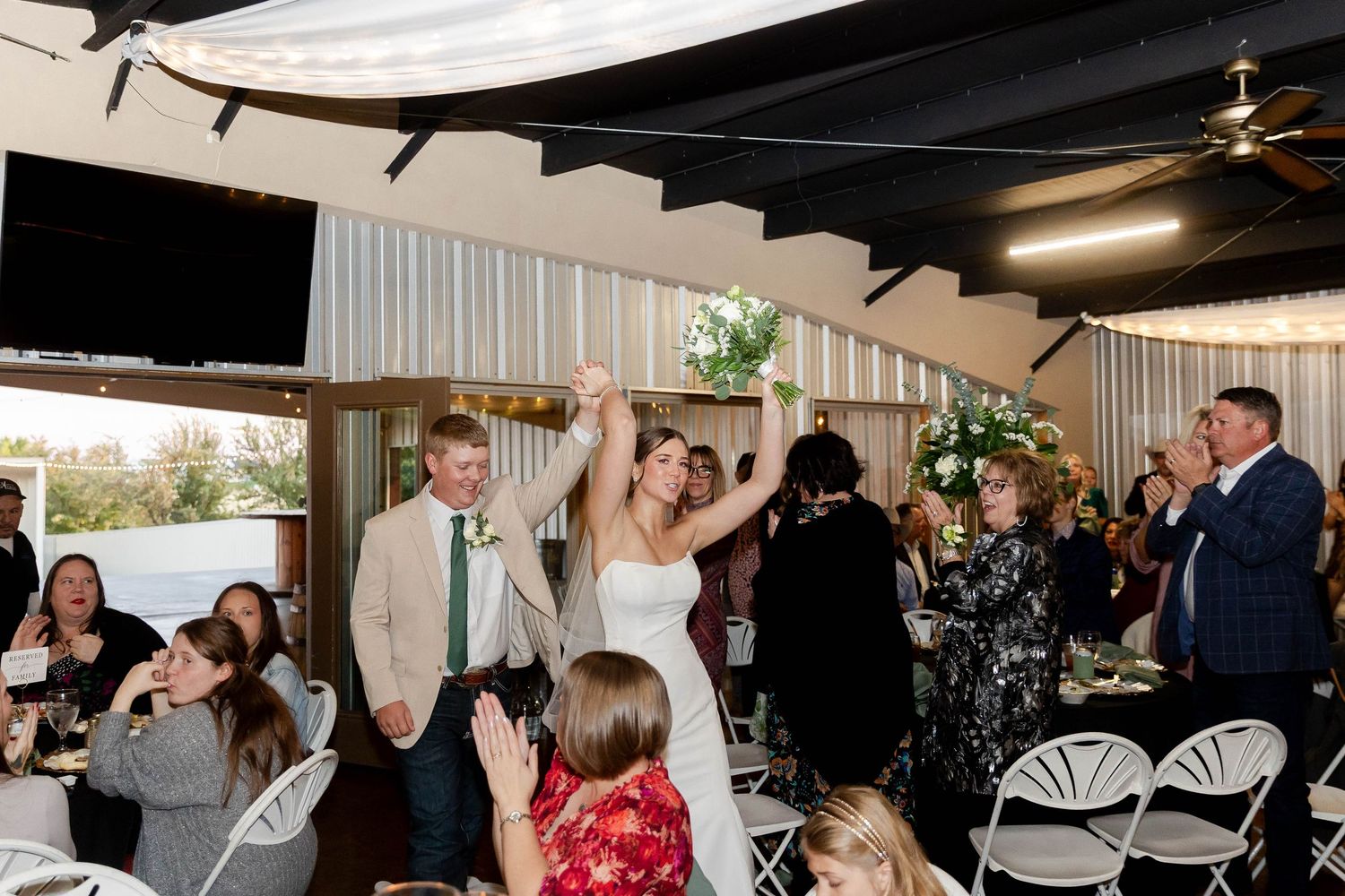 Wedding reception guests dance and celebrate under indoor venue lighting.