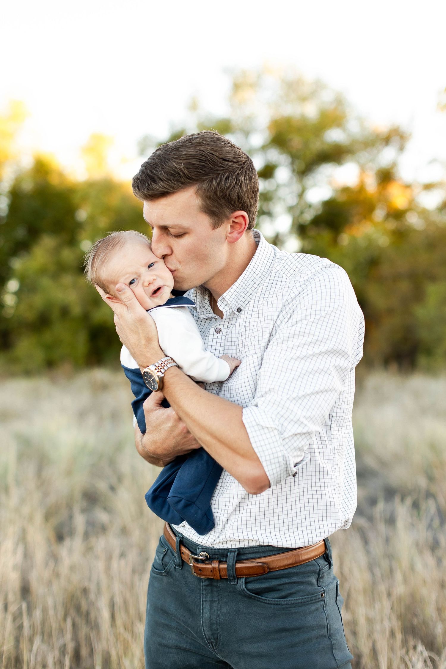 Father and young child share affectionate moment in field at sunset.