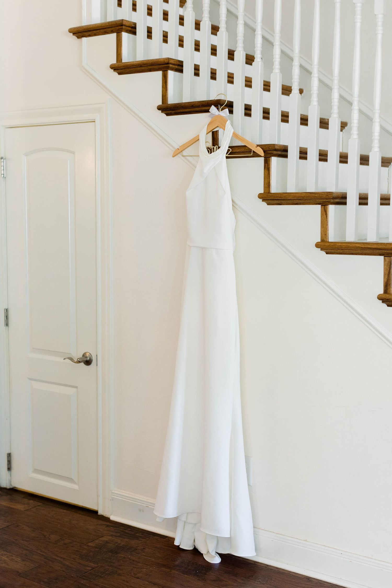 A white wedding dress hangs elegantly against a classic white staircase with wooden details.