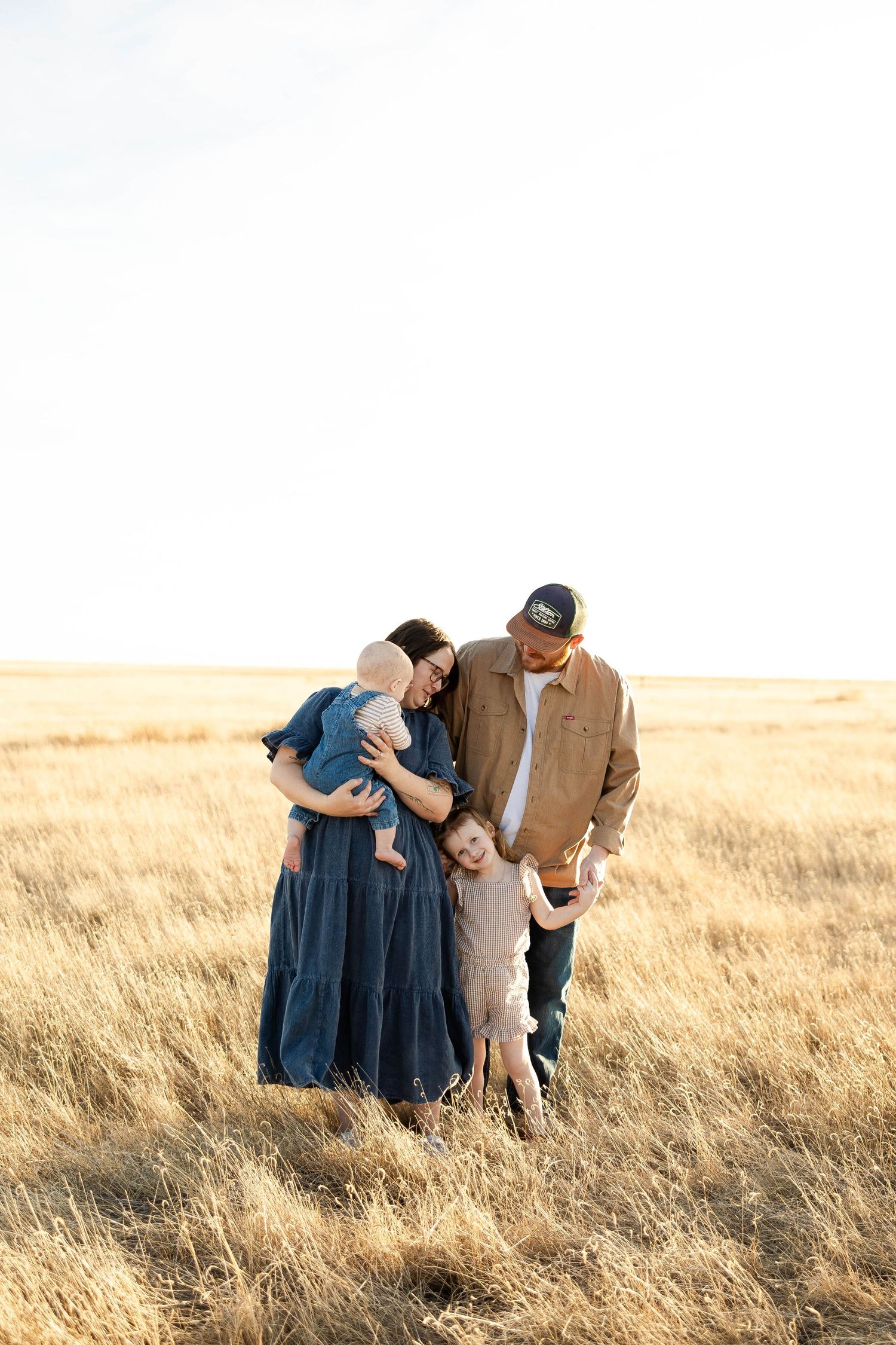 A family shares a tender moment together while standing in a golden wheat field at sunset.