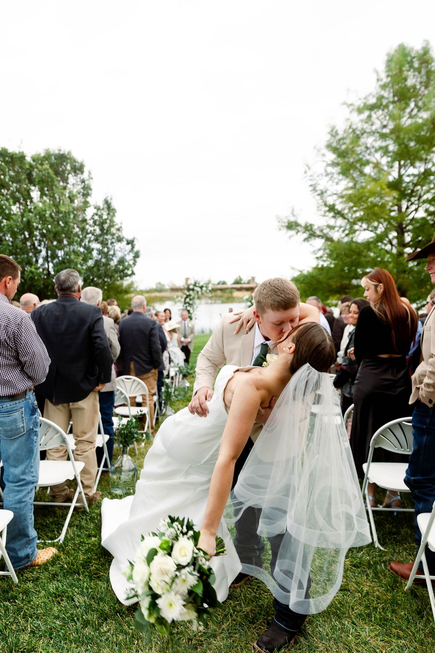 Wedding guests gathered on a grassy lawn with white folding chairs at an outdoor ceremony.