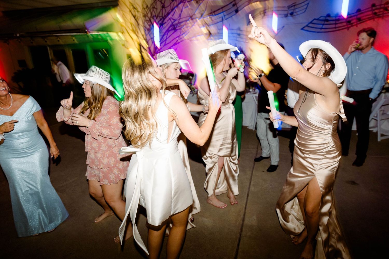 Wedding reception guests dancing and celebrating on a colorful dance floor with vibrant lighting.