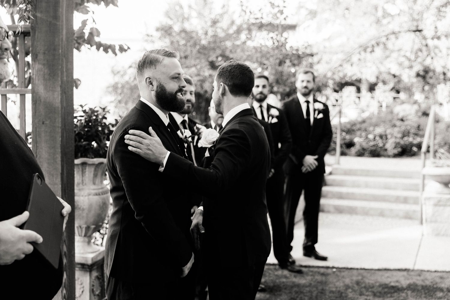 Black and white photo of wedding guests gathered outdoors under trees during a ceremony.
