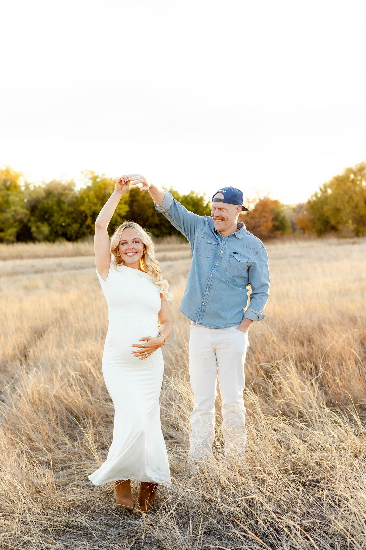 A couple dances together in a golden field during sunset wearing casual attire.
