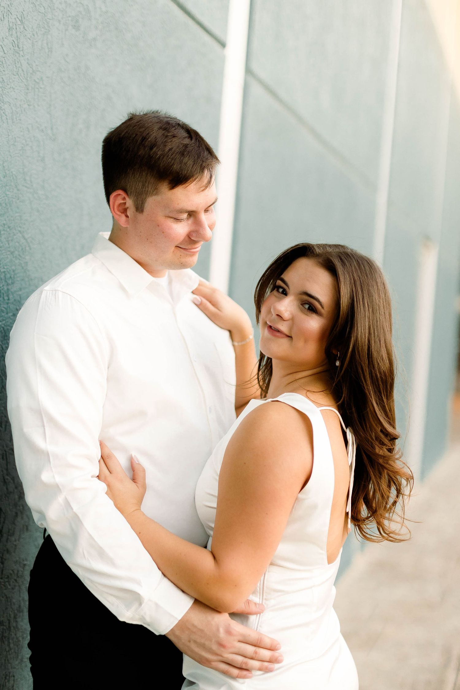A couple shares intimate moments against a modern architectural backdrop in an engagement photoshoot.