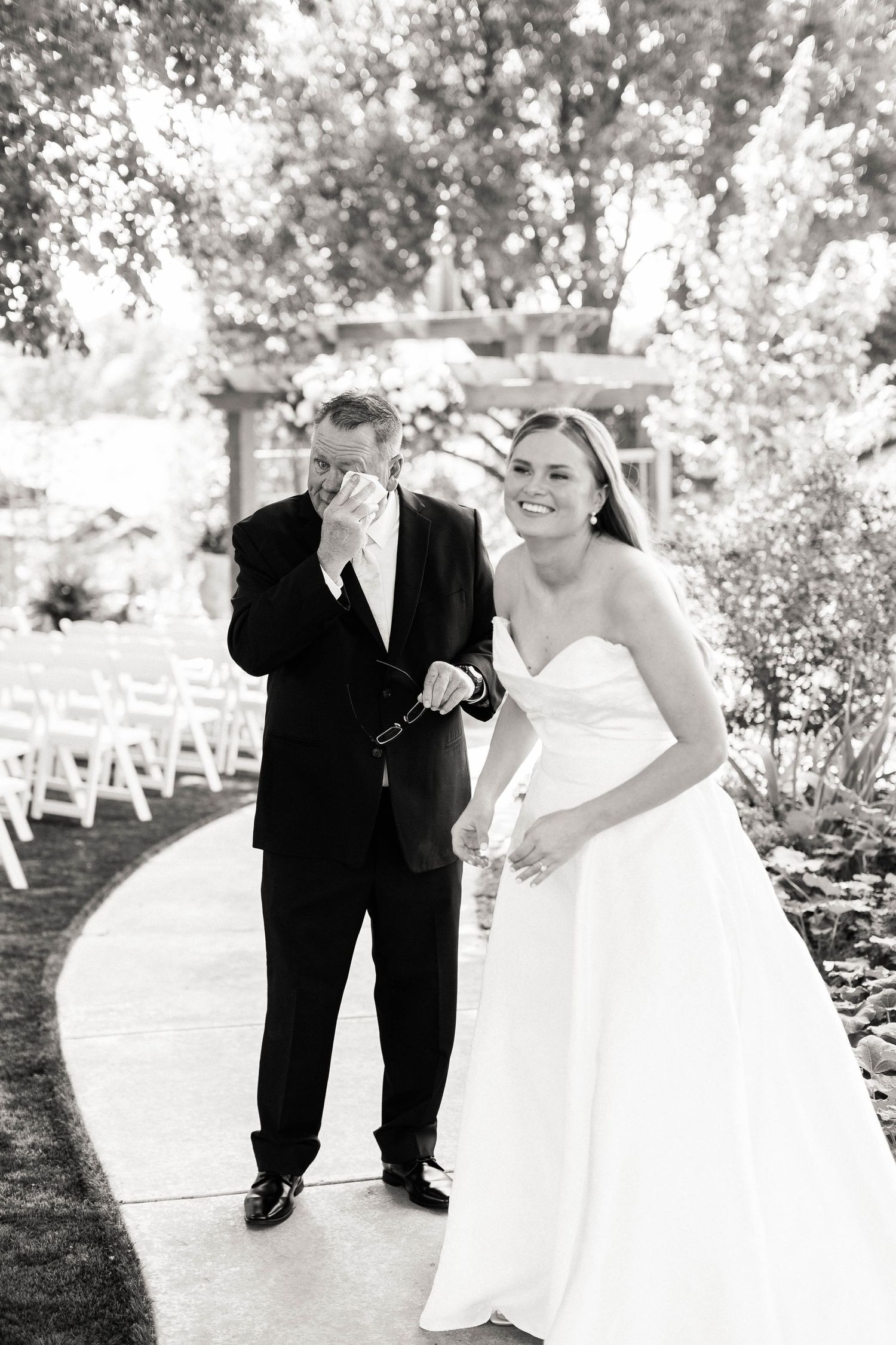 Black and white wedding photo series showing couple dancing playfully outdoors with trees and chairs in background.
