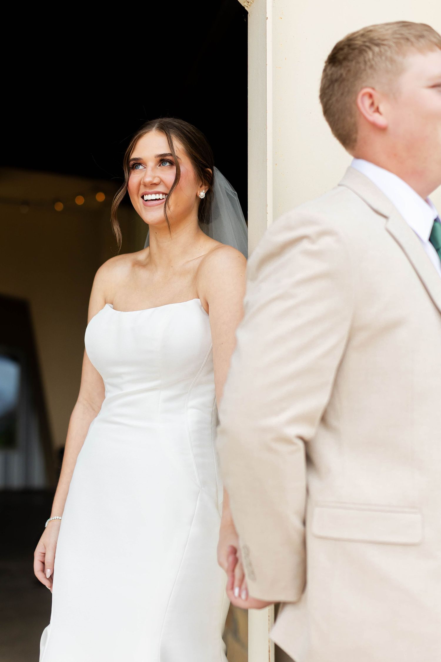 A couple in wedding attire, with the bride in white and groom in cream colored suit, share a tender moment.