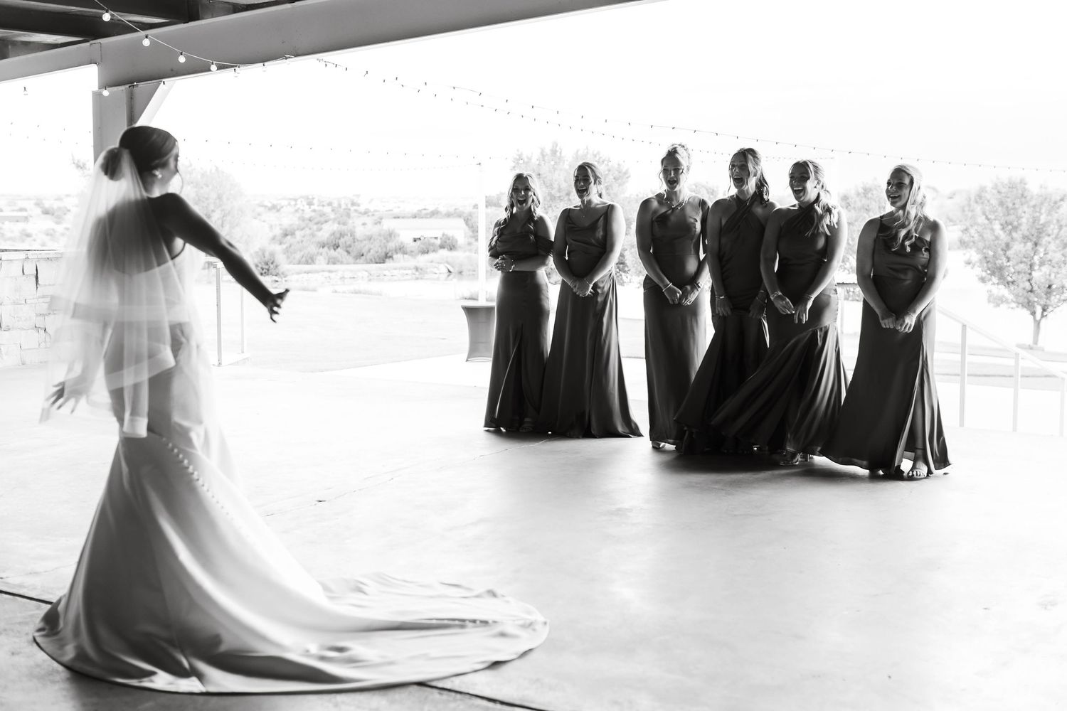 Black and white panoramic wedding photo showing a bridal party arranged in a minimalist modern setting.