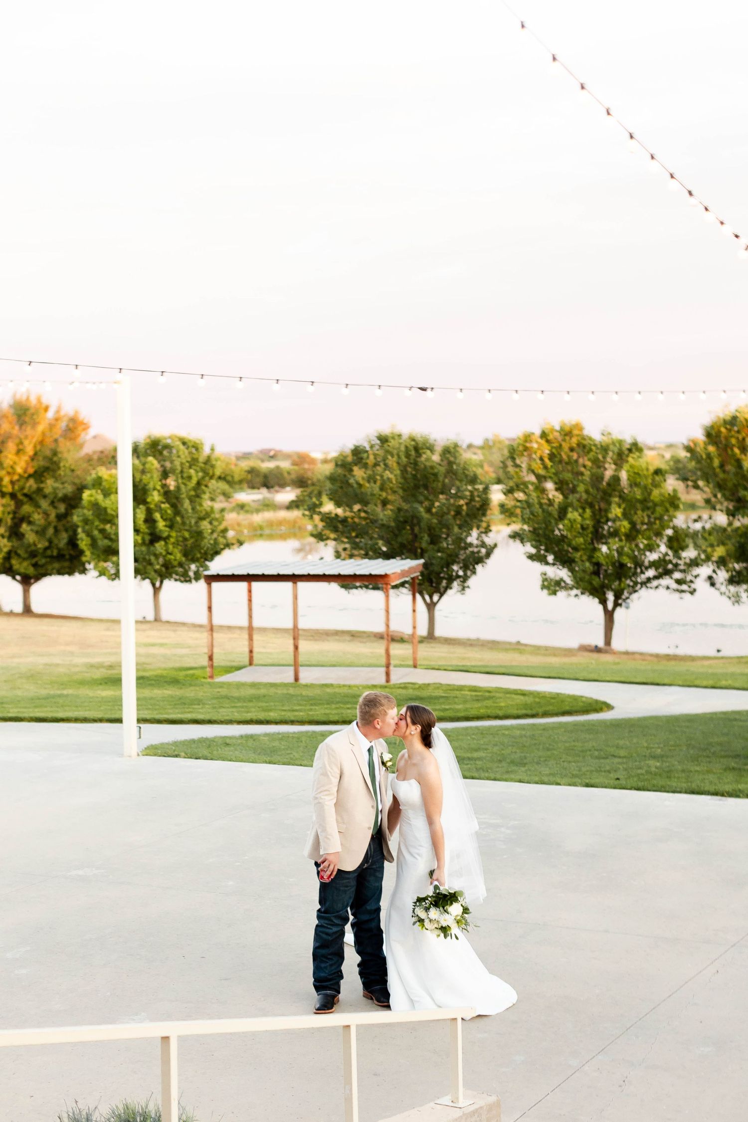 Outdoor wedding venue with string lights and waterfront view at sunset.