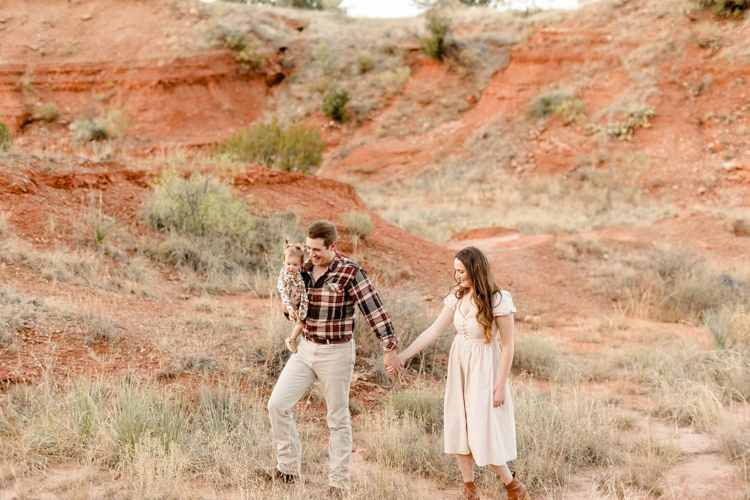 A couple explores red rock formations in casual attire during a desert photoshoot.