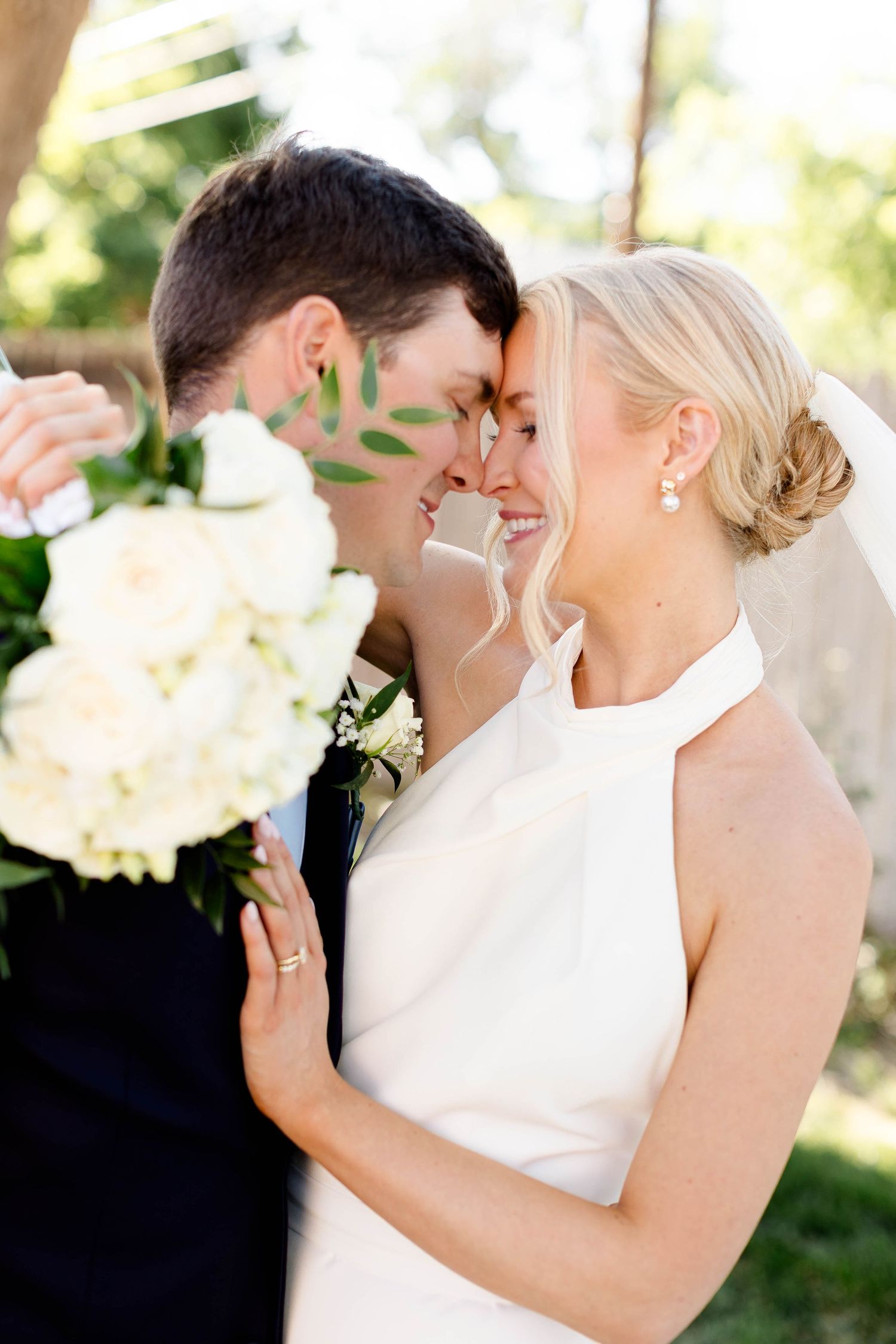 Close-up wedding photo of a couple sharing a tender moment with white flowers in the foreground.
