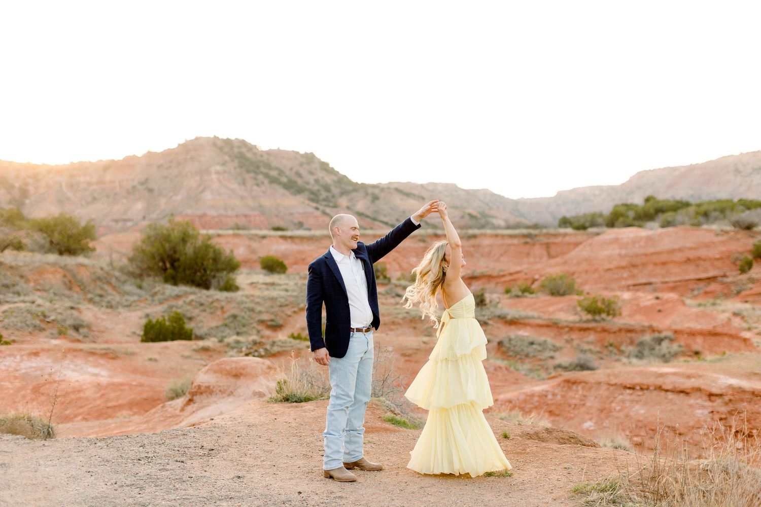 A romantic desert photoshoot featuring a couple walking together on red rock terrain.