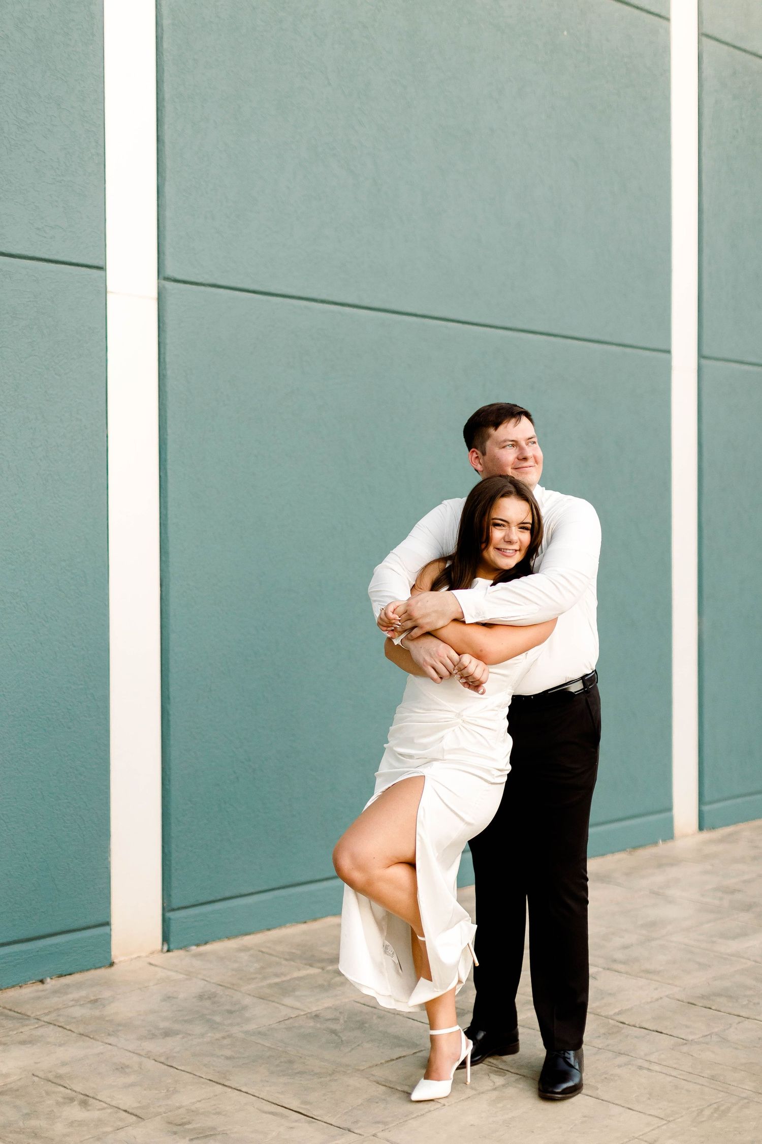A couple in formal wear creates dynamic poses against a modern architectural backdrop.