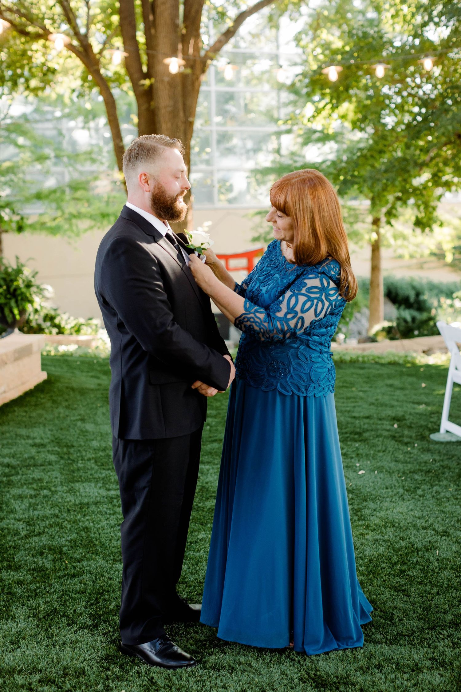 Two wedding guests share a joyful dance moment on grass under trees.