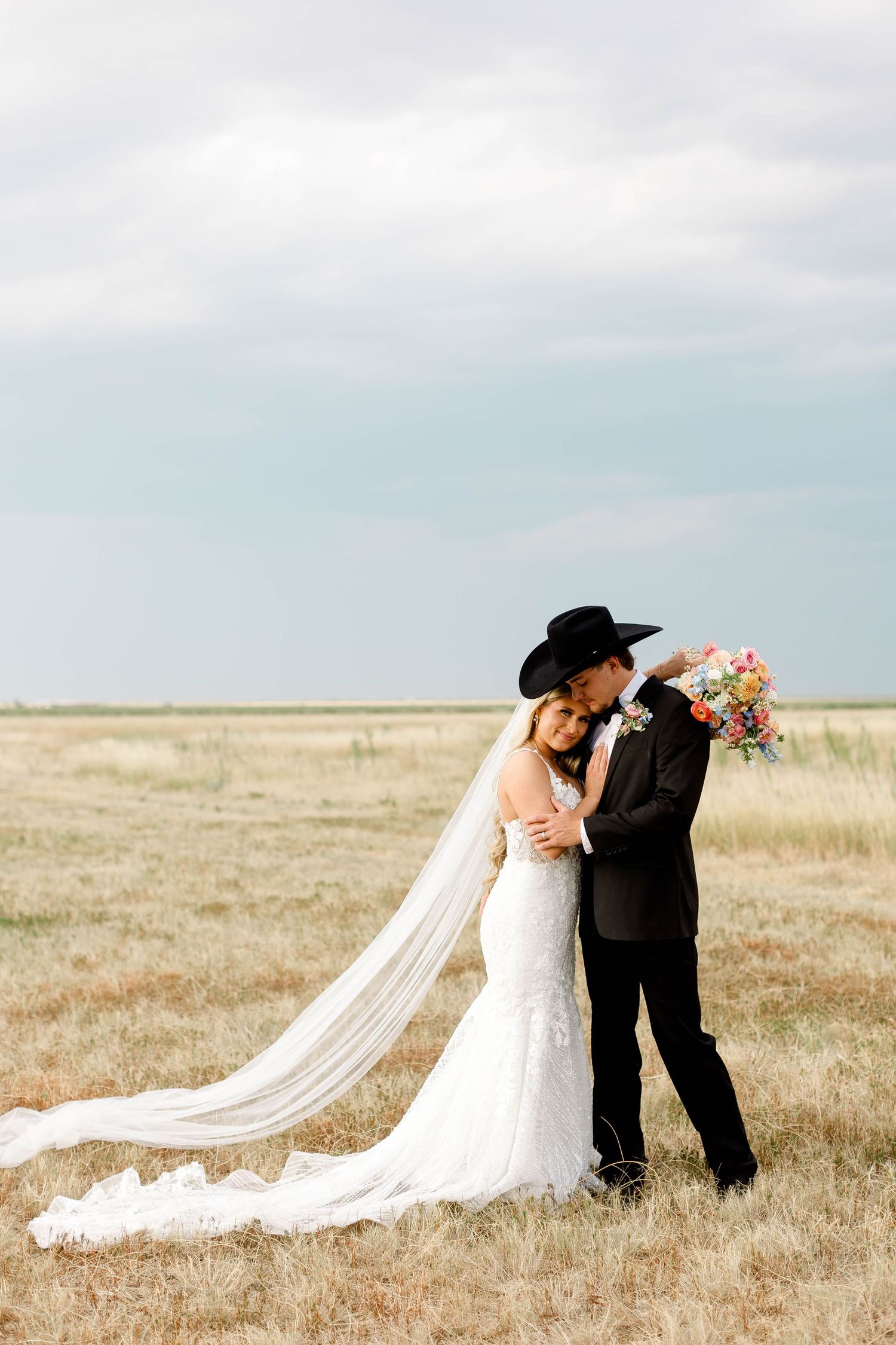 Wedding couple shares romantic moments in a rustic field with dramatic flowing veil.