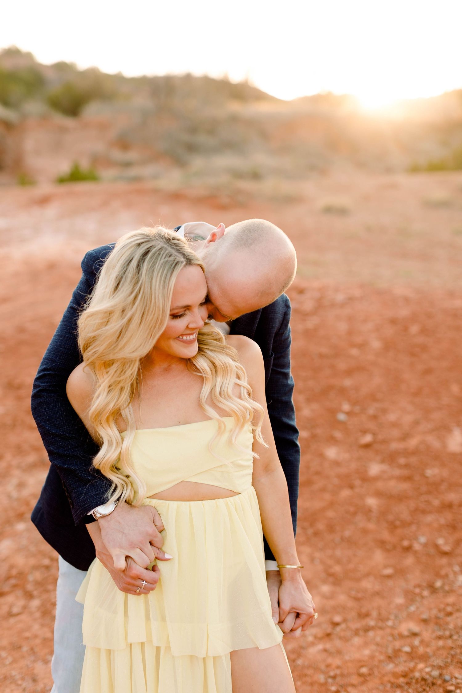 A romantic moment captured between a couple in formal wear against a desert landscape at golden hour.