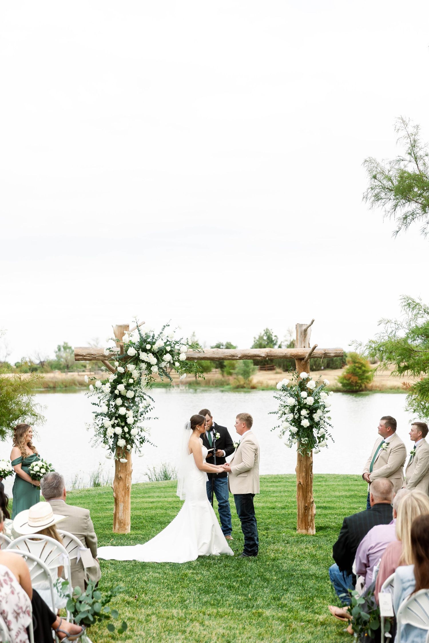 An outdoor wedding ceremony setup with white floral arrangements and wooden arch near a waterfront.