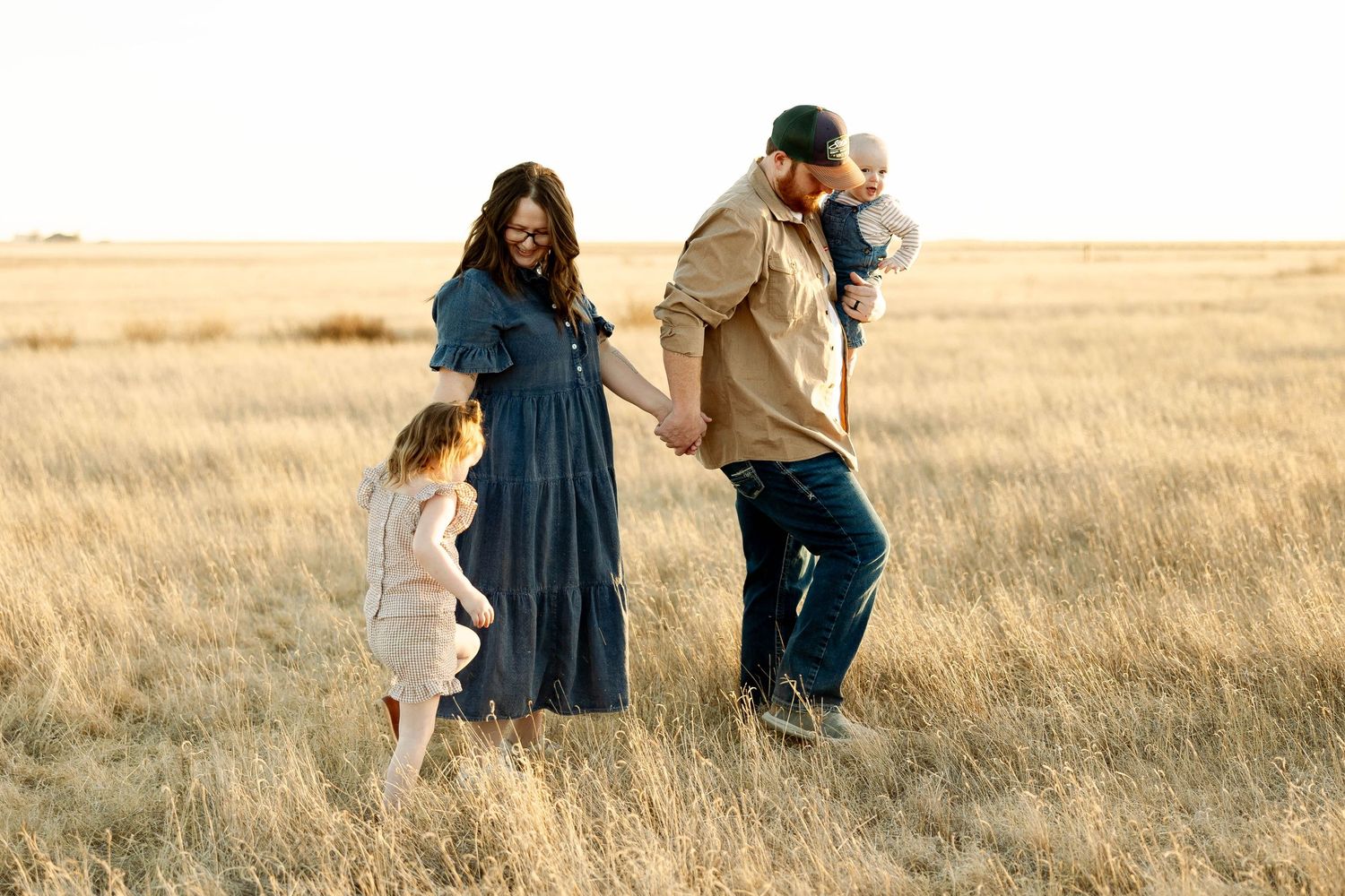 A family walks together through a golden wheat field at sunset in casual attire.