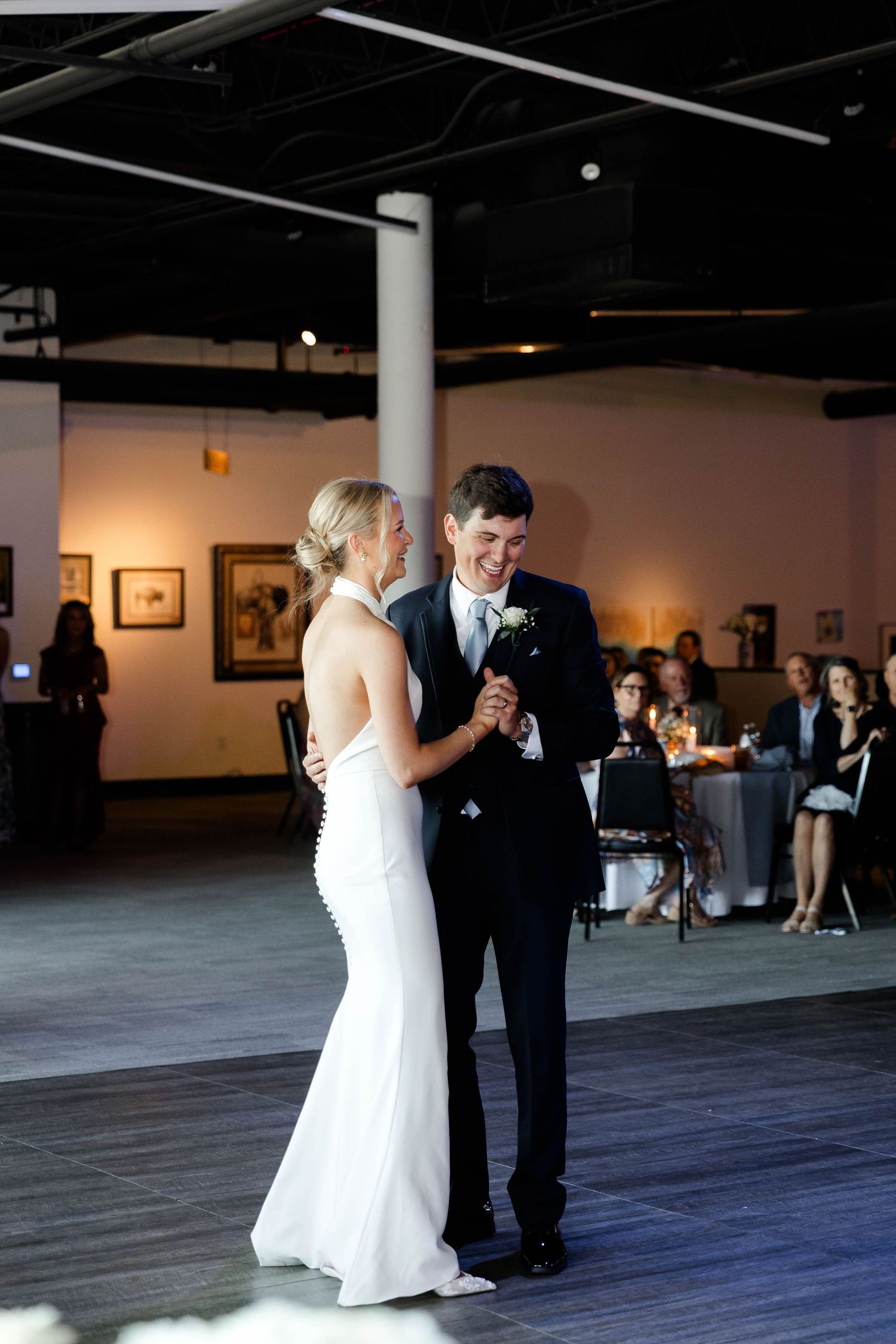 Wedding couple sharing their first dance in a gallery space with artwork on walls.