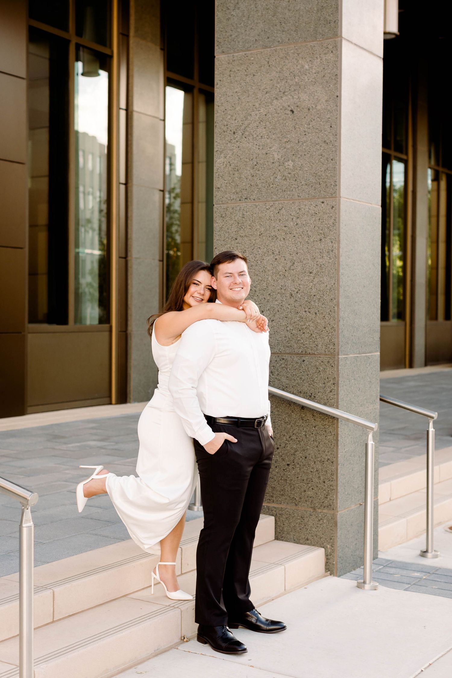 Joyful couple in formal wear embracing on steps of modern building.