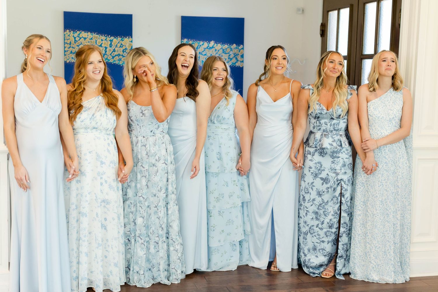 Bridesmaids wearing light blue dresses stand in a row showing off their elegant coordinated wedding attire.