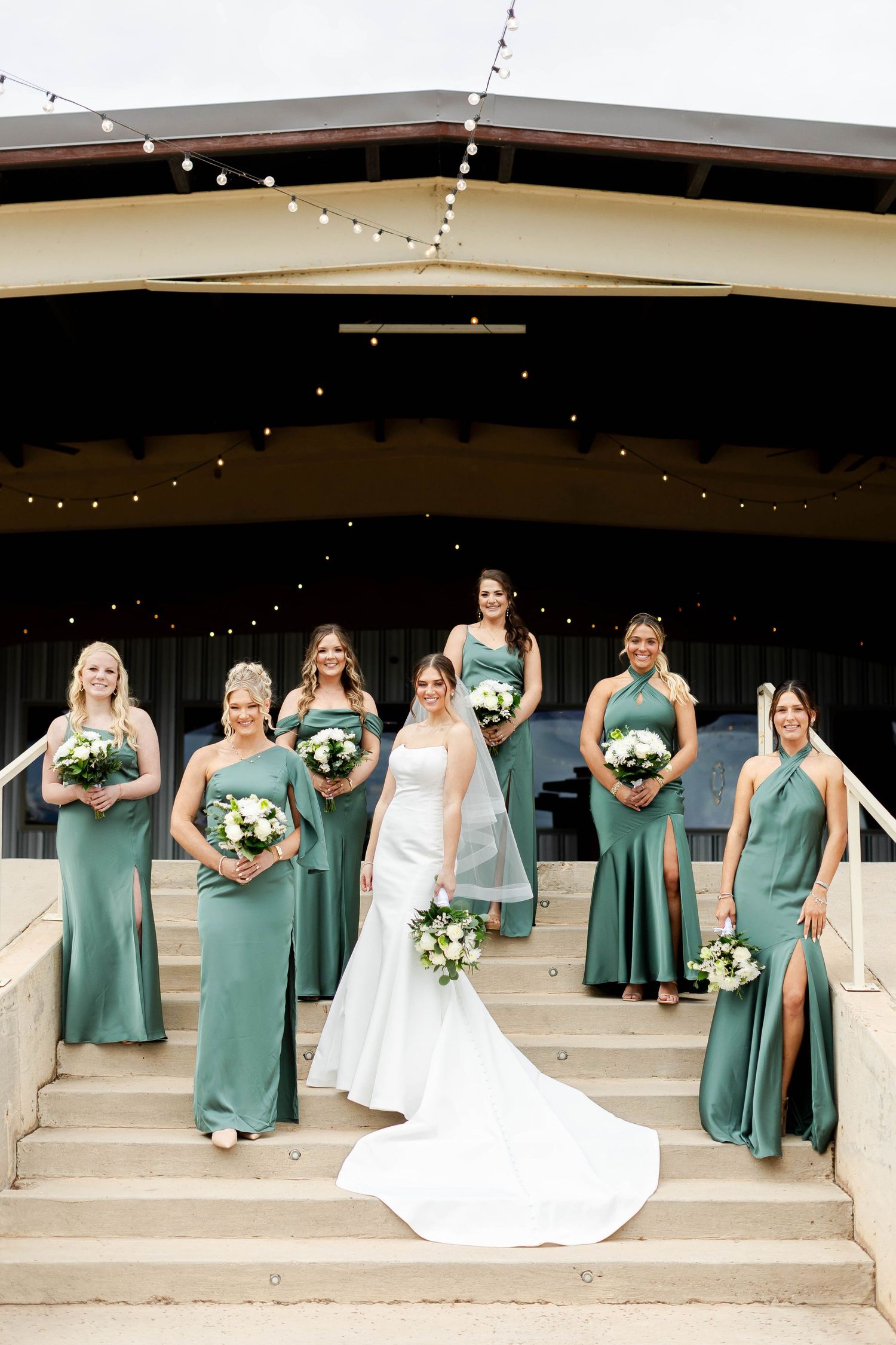 Wedding party creates fun photo lineup on concrete steps with bridesmaids in sage green dresses.