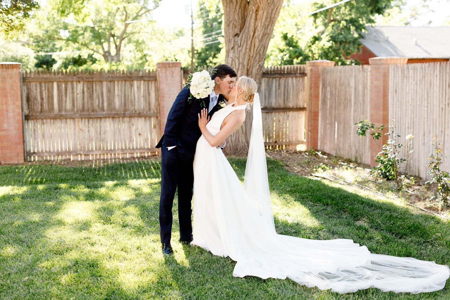 Elegant wedding couple posing in a garden with wooden fence backdrop.