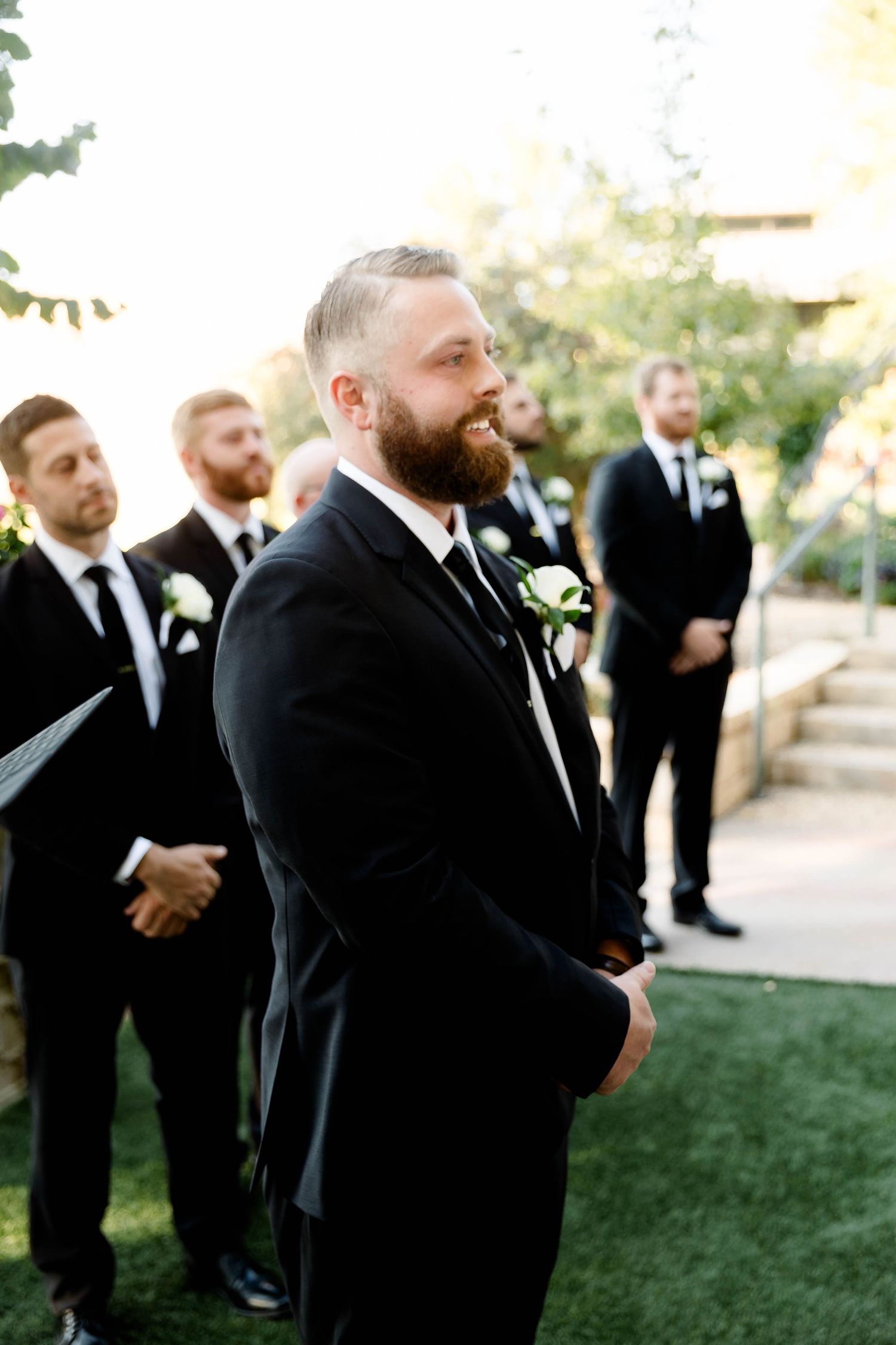 Wedding party members in black suits gathered outdoors during a formal ceremony.