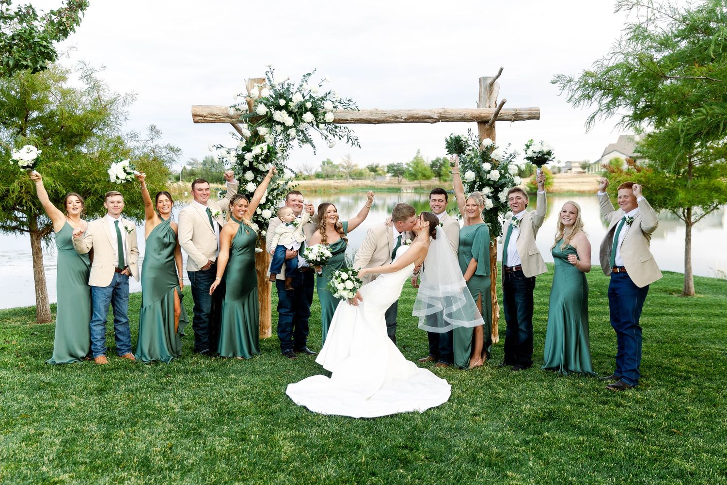 Outdoor wedding ceremony setup with wooden cross altar and guests gathered on a grassy field.