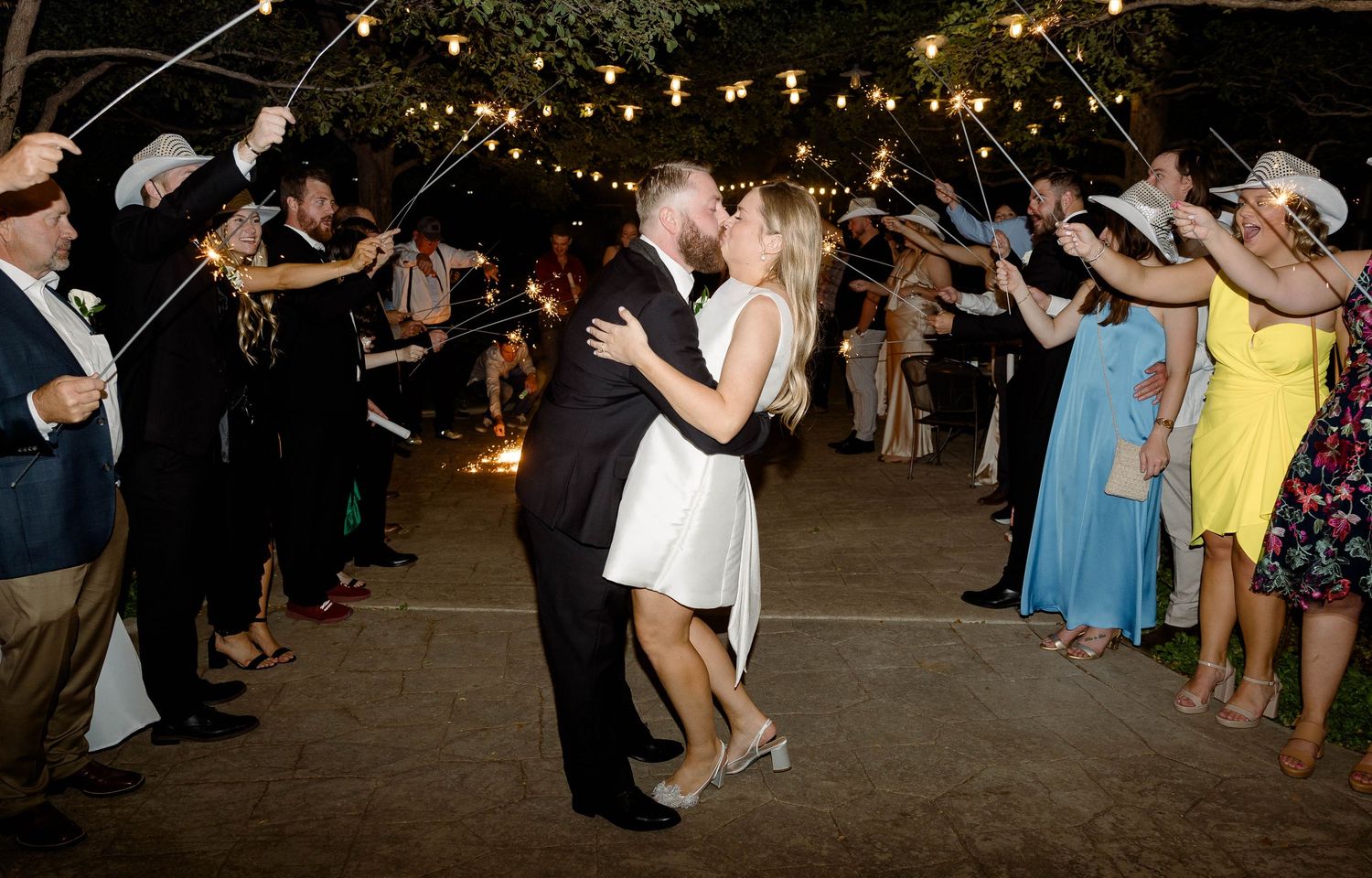 Wedding guests dancing under warm string lights at an outdoor evening celebration.