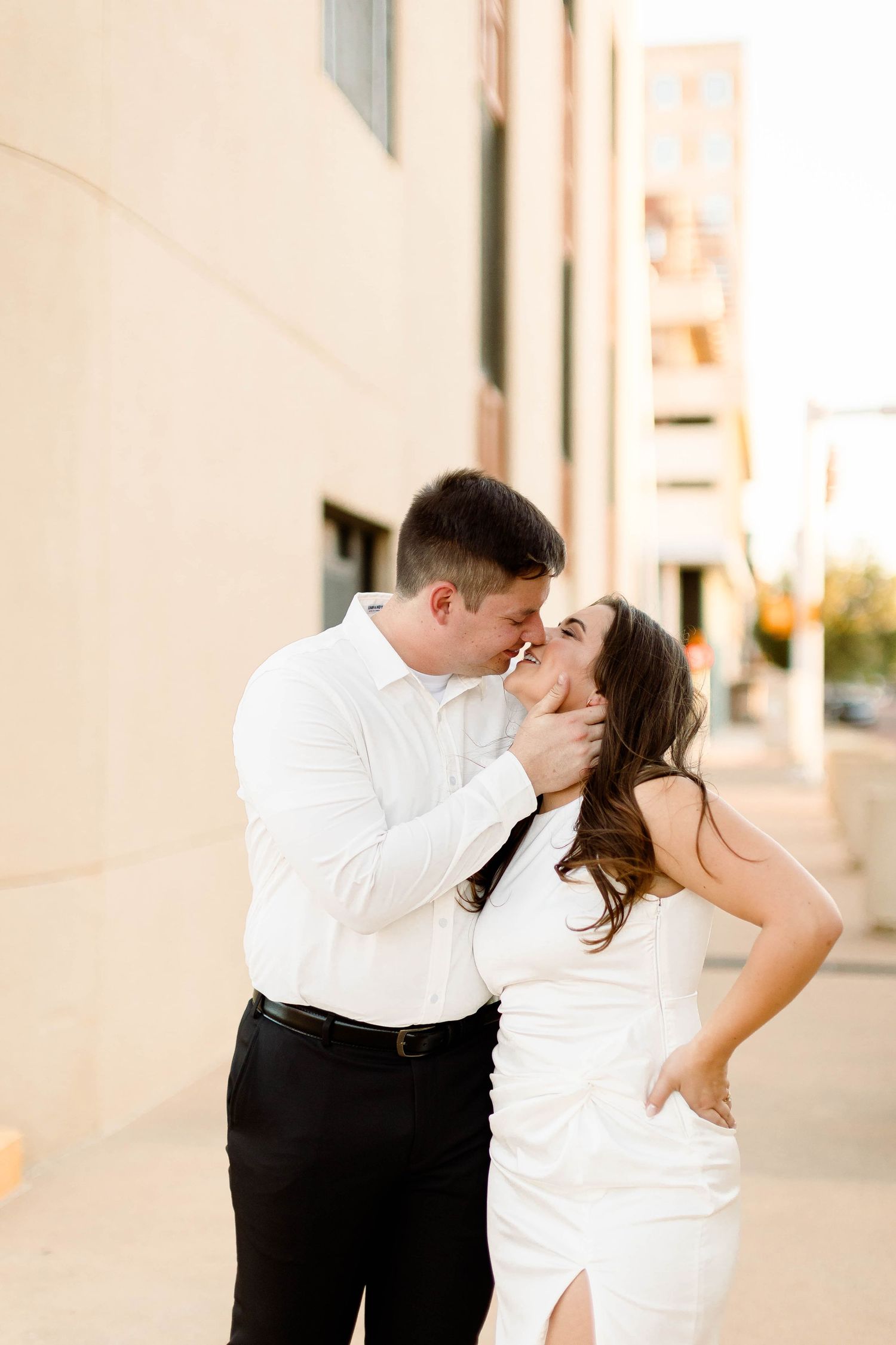 A romantic couple shares a tender kiss while dressed in formal white and black attire.
