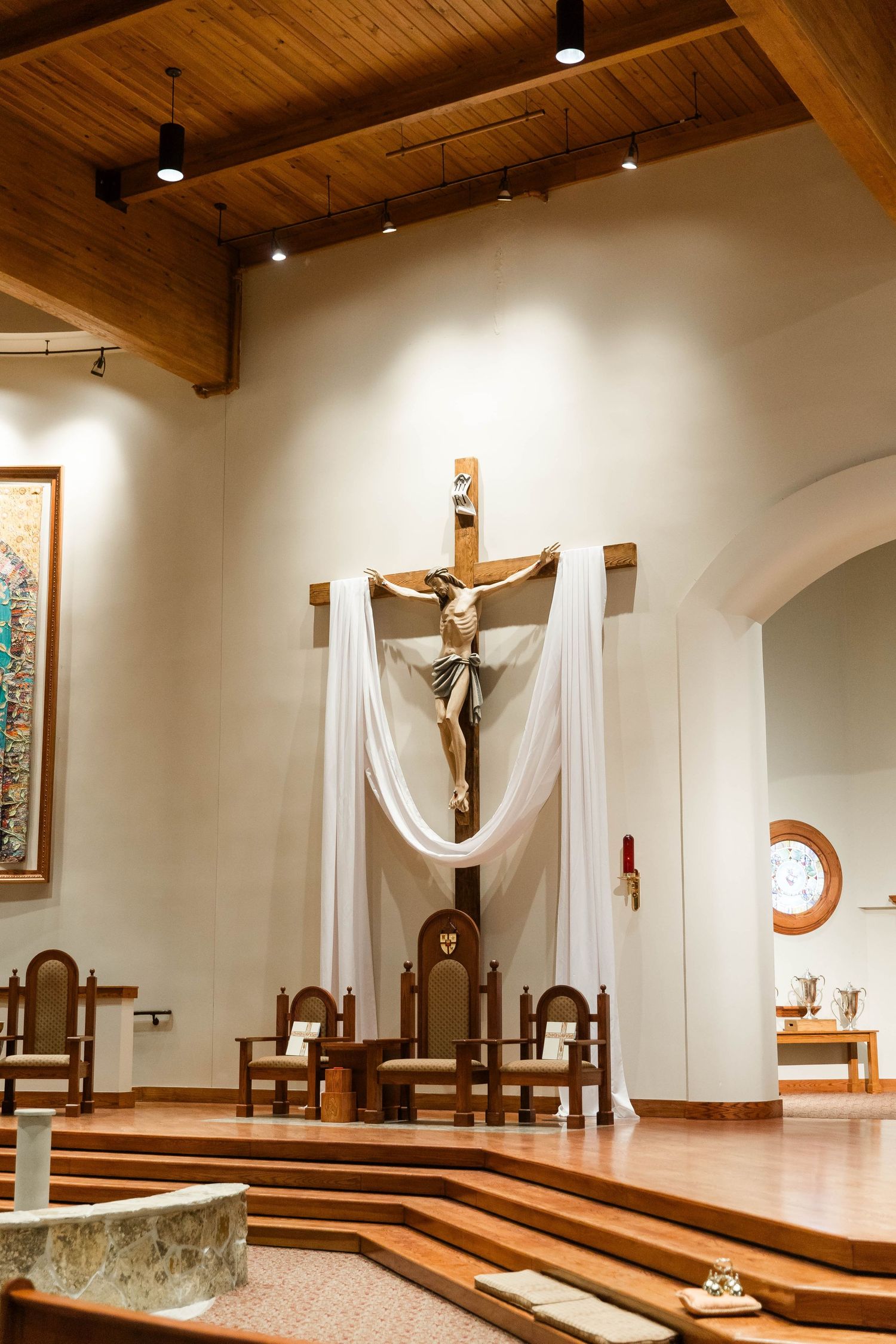 Modern church altar area with crucifix, white drapes, and tiered wooden platforms.