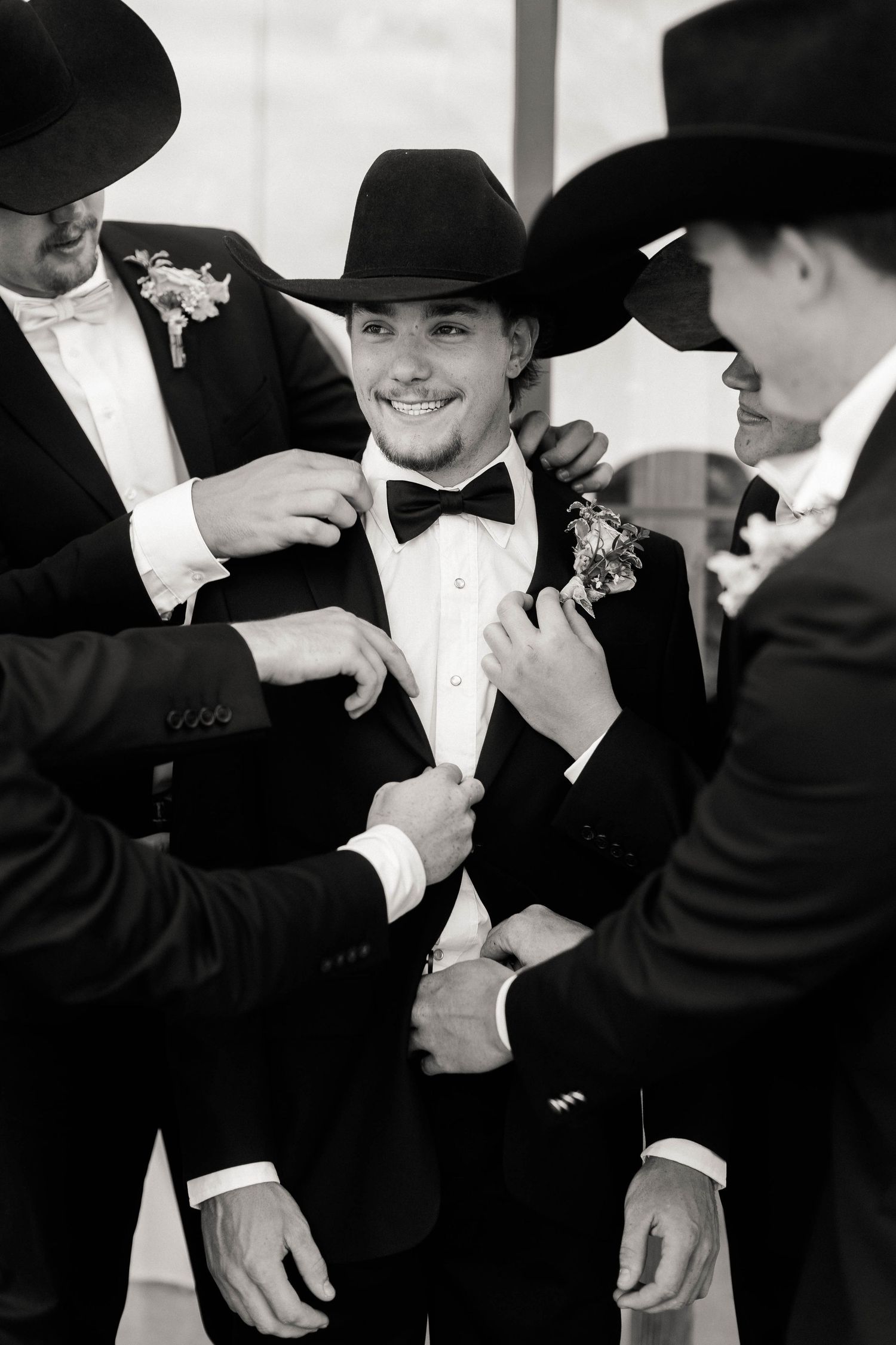 Sequence of groomsmen in black cowboy hats helping each other with formal attire.