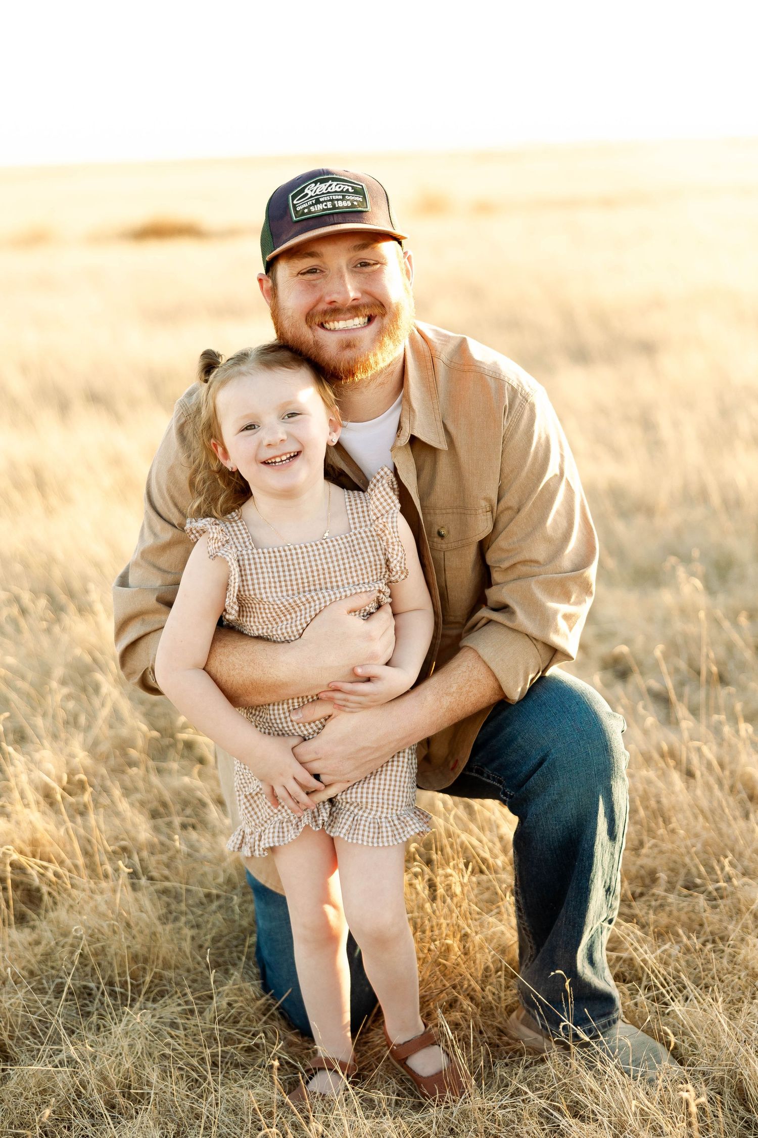 A parent and child share joyful moments together in a golden wheat field at sunset.