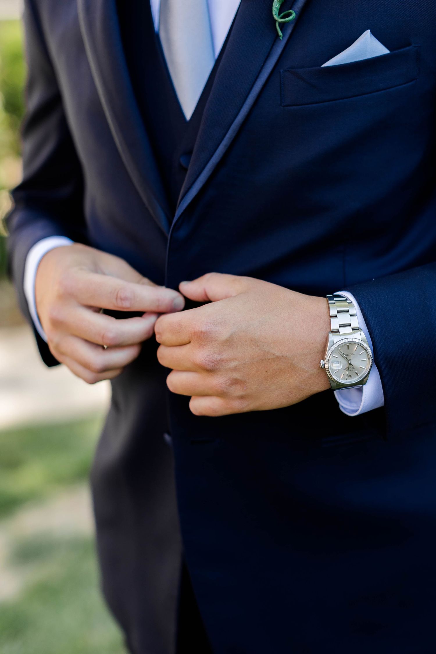 Close-up detail of a navy suit jacket with pocket square and silver watch.
