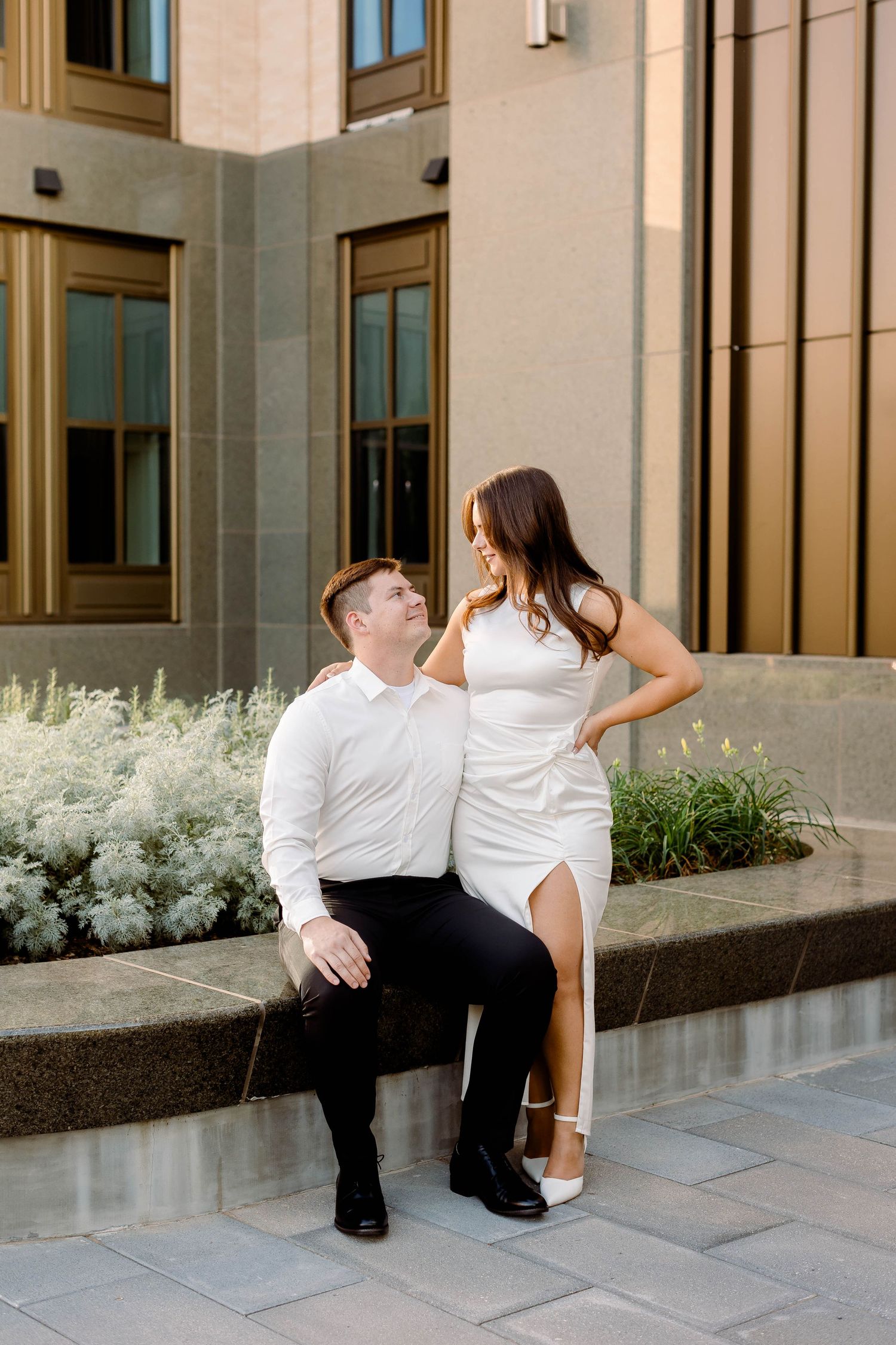 Playful couple in formal wear interacts on modern building steps.
