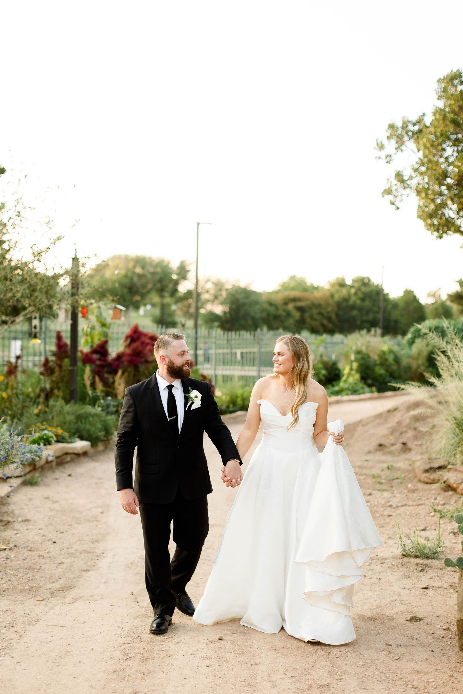 Newlywed couple walking hand in hand along a desert path during sunset at their outdoor wedding celebration.