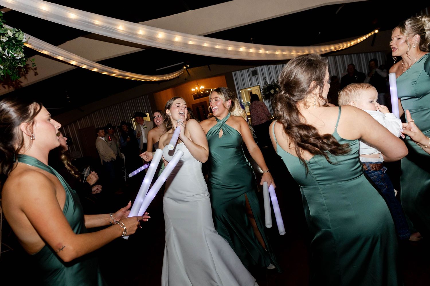 Wedding guests dancing and celebrating at an indoor reception with mood lighting.