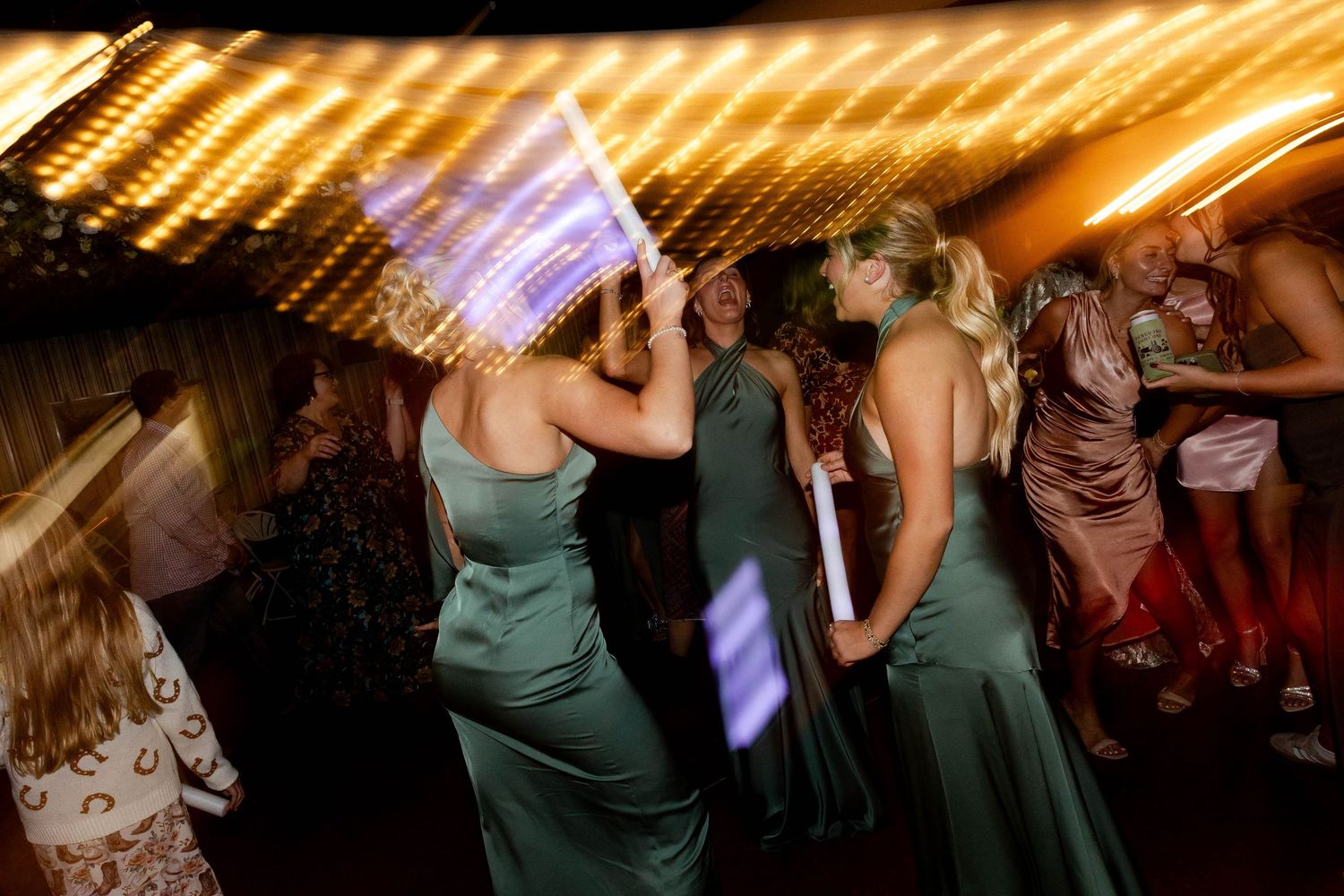 Dance floor celebration with warm lighting and guests in emerald green dresses.