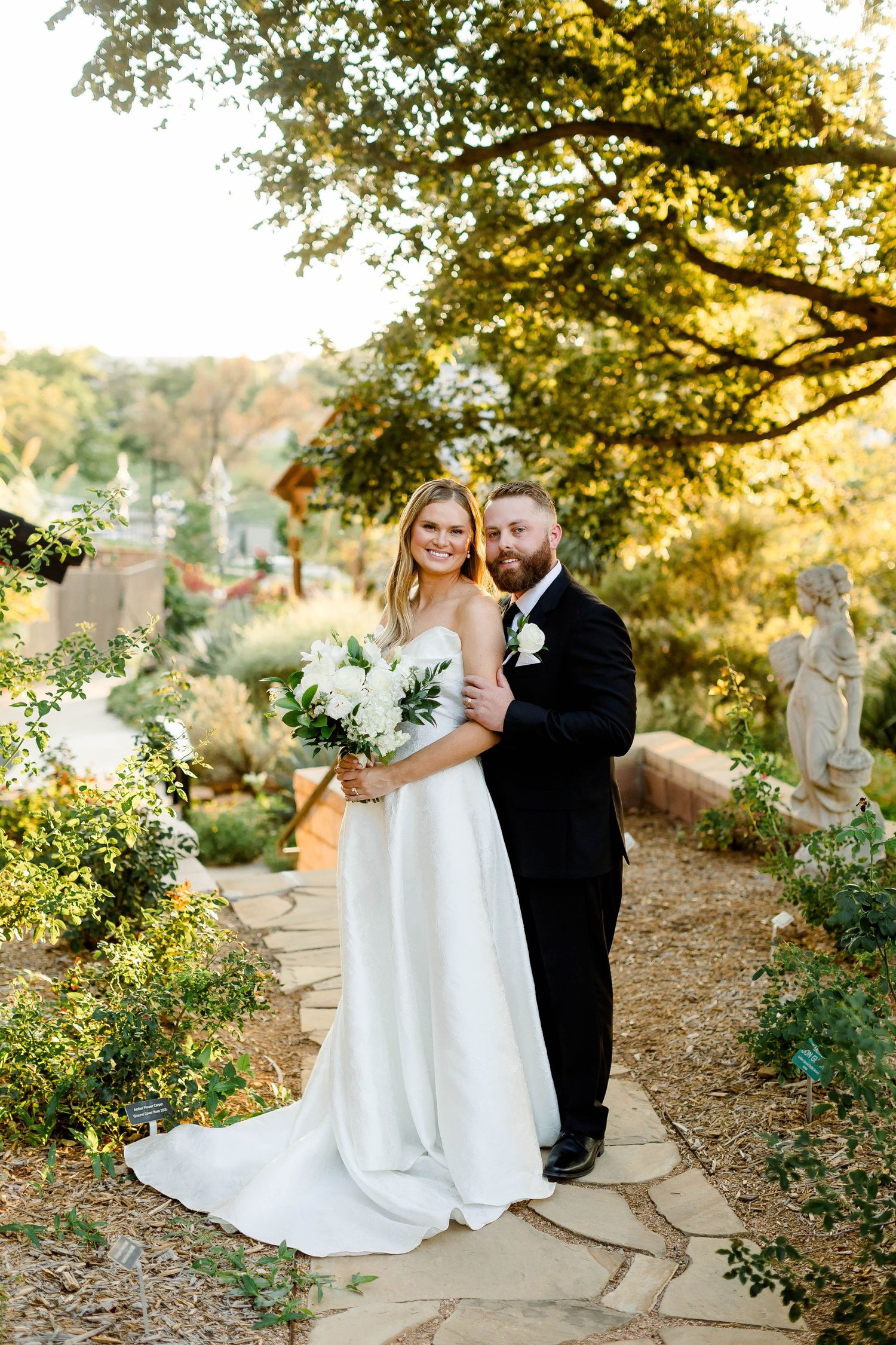 A couple poses together on a stone path surrounded by lush greenery at sunset.