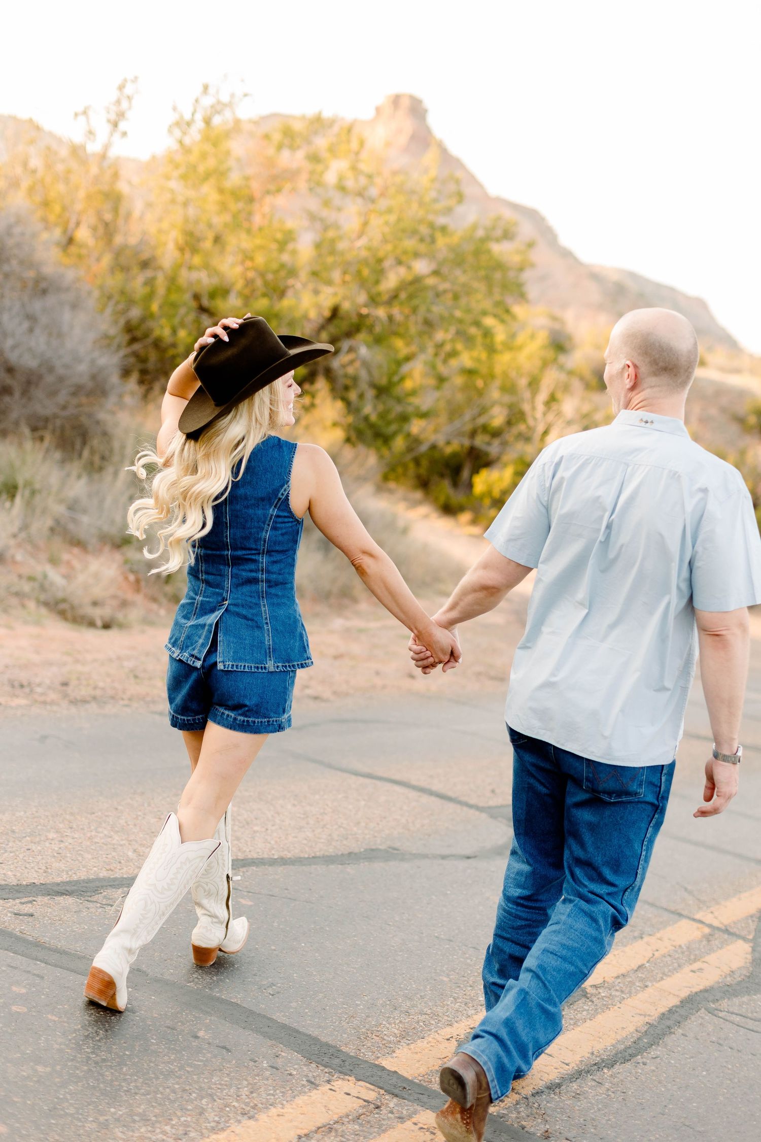 Couple walking hand in hand on desert path during sunset with mountains in background.